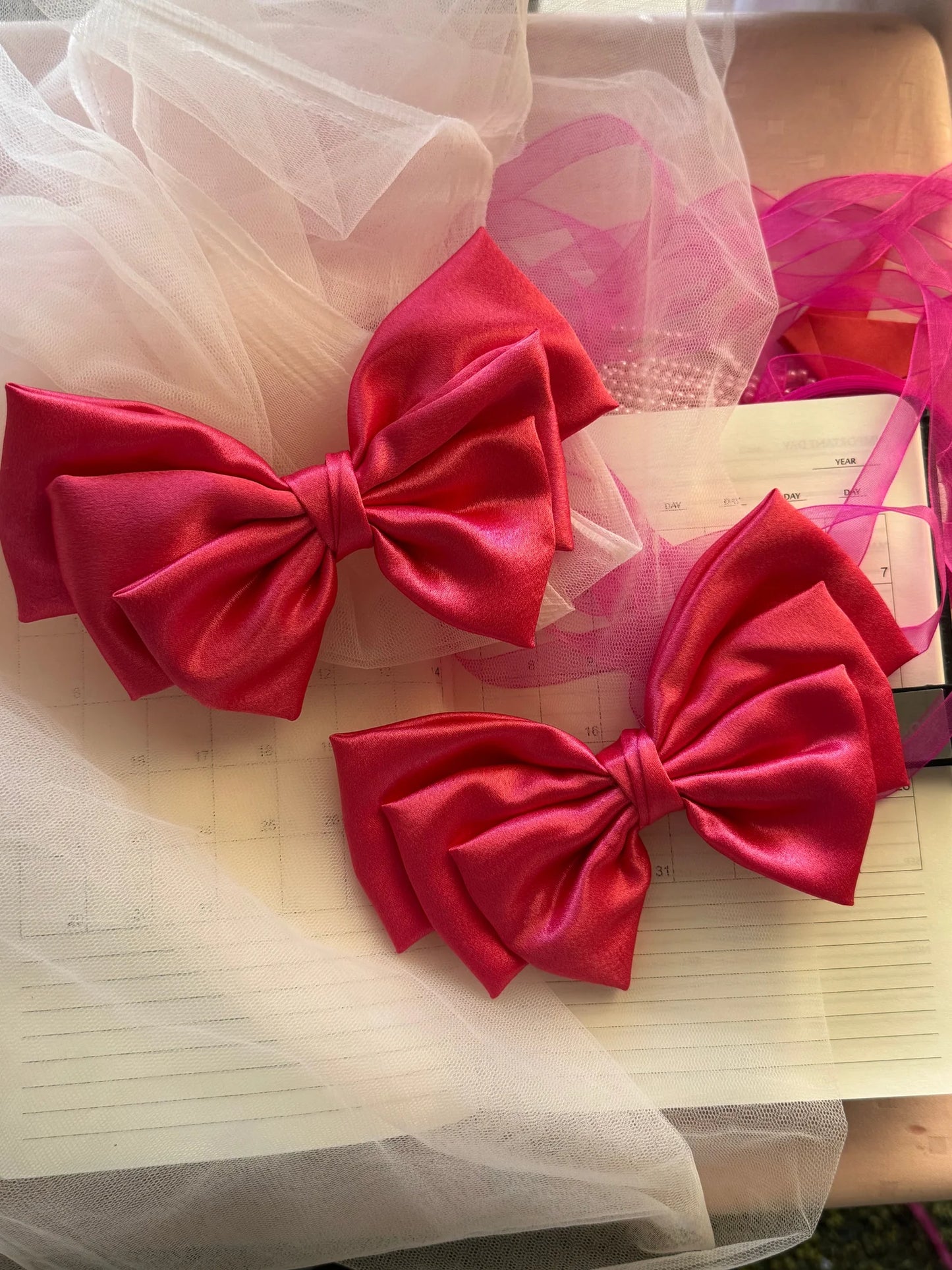 Hot pink satin hair bows by Bows and Bags India displayed on cream notebook with tulle fabric, showing handmade texture and
