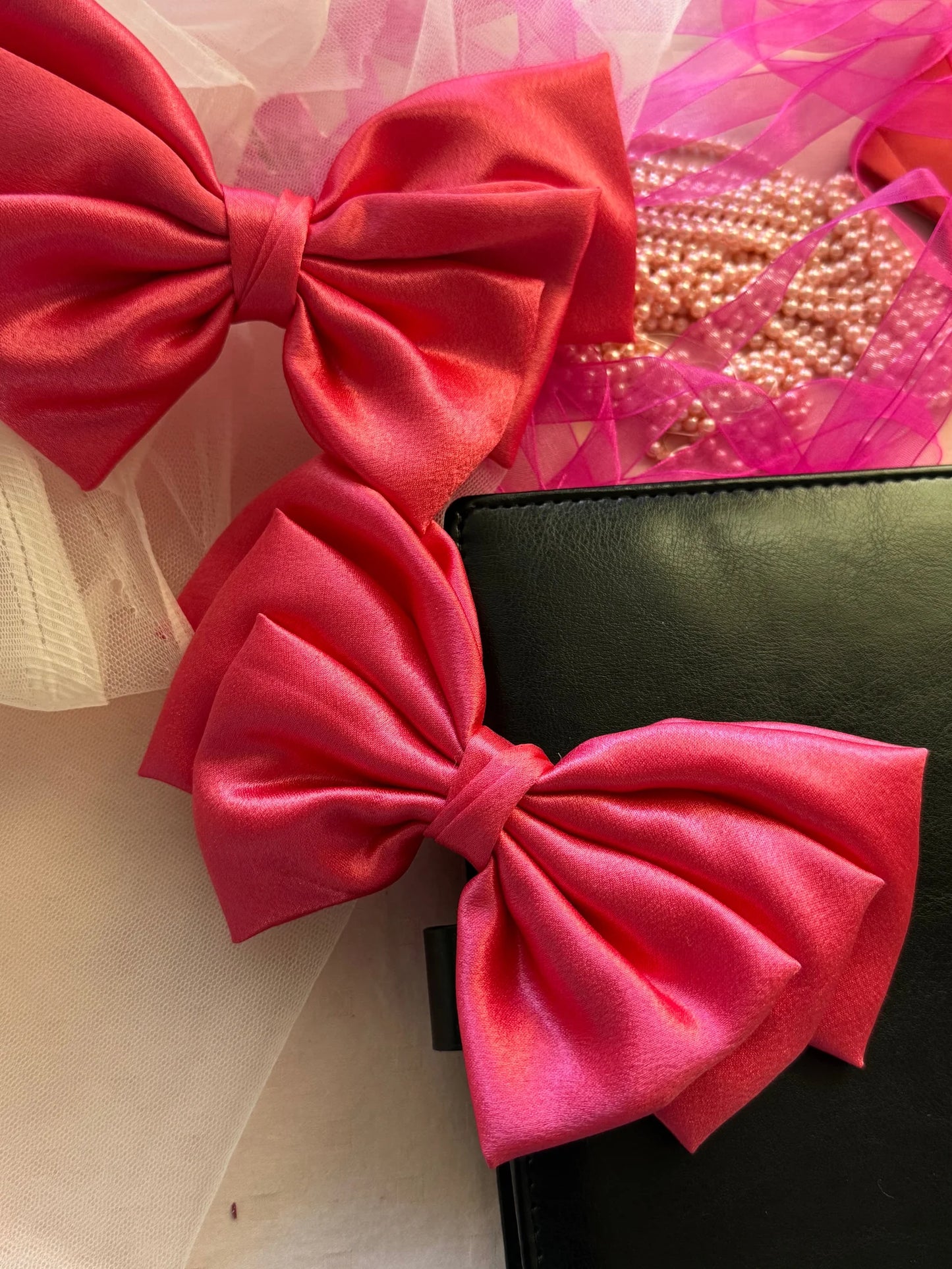 Hot pink satin hair bow with alligator clip by Bows and Bags India, displayed with pearl beads and black wallet accessory