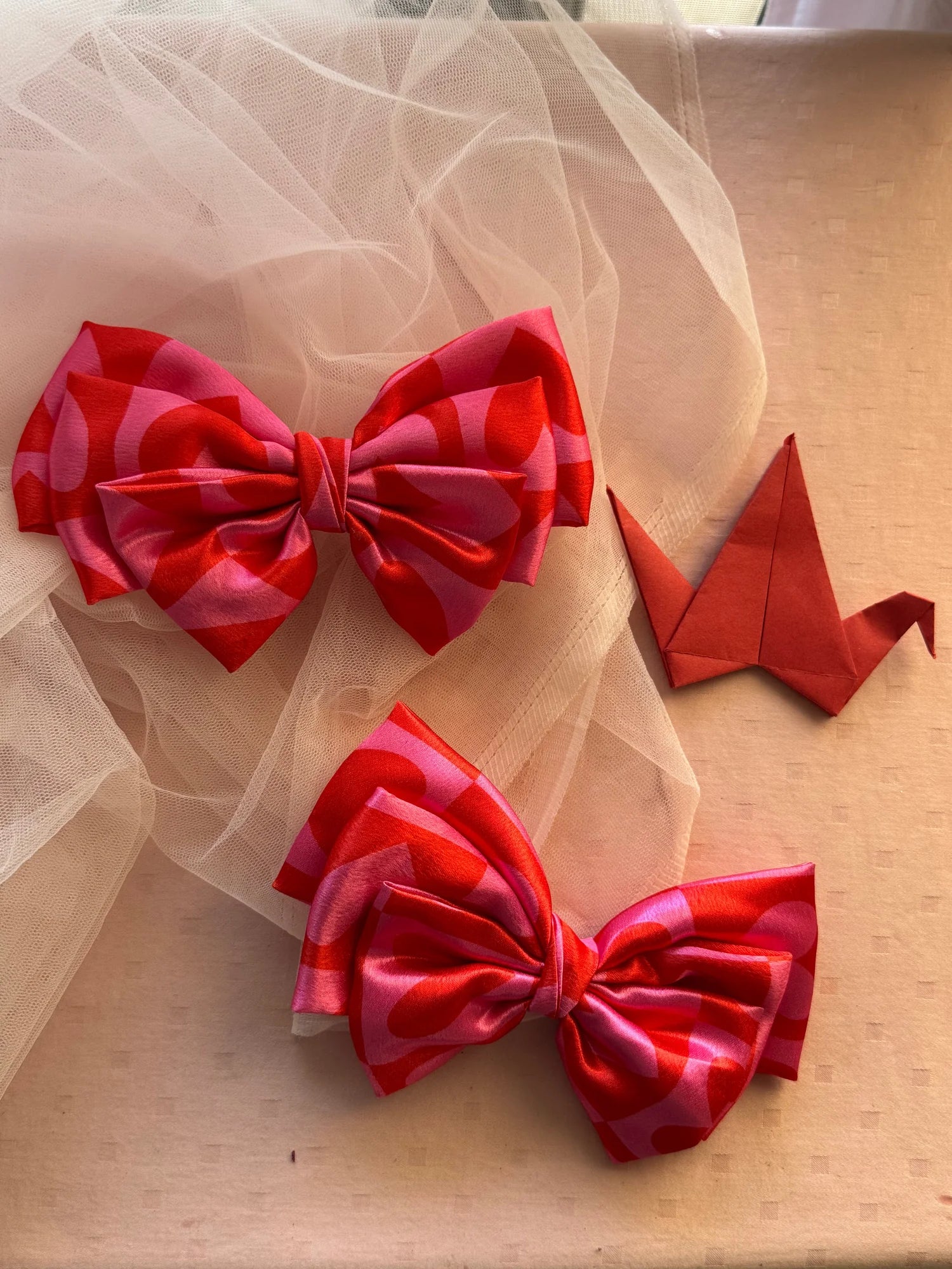 Pink printed satin hair bow with heart pattern by Bows and Bags India, displayed on tulle fabric with origami crane detail