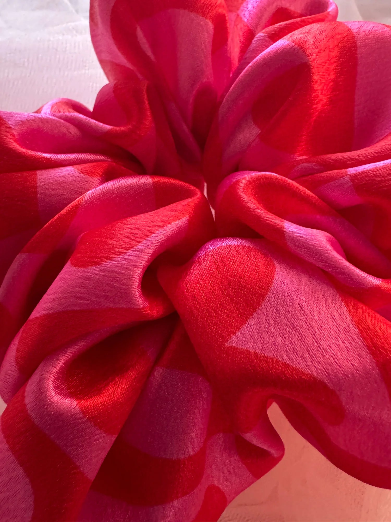Close-up of Love Stuck satin scrunchie showing luxurious pink heart-printed fabric texture and layered folds by Bows and