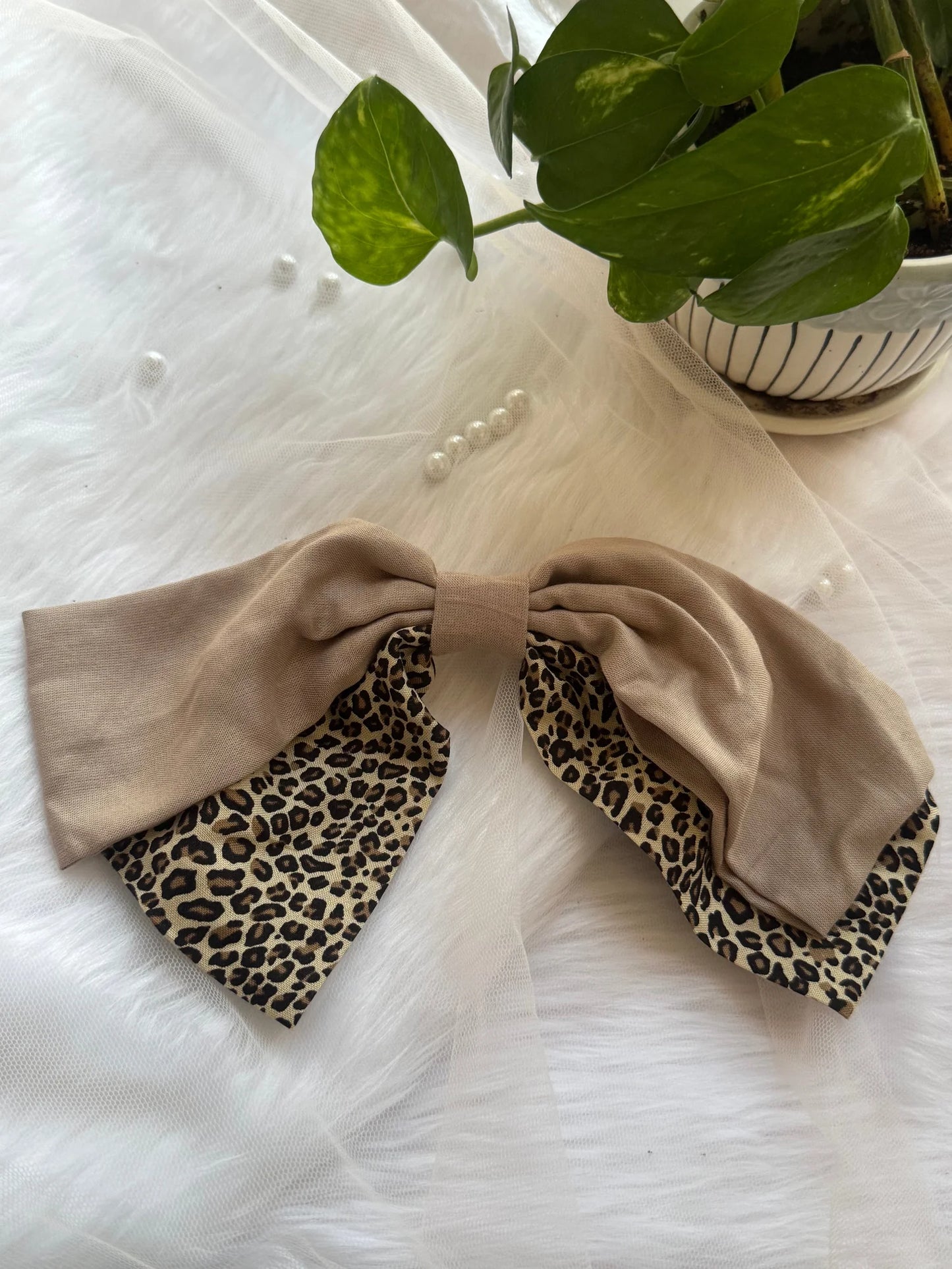 Beige and leopard print Madonna hair bow by Bows and Bags India displayed on white textured background with potted plant
