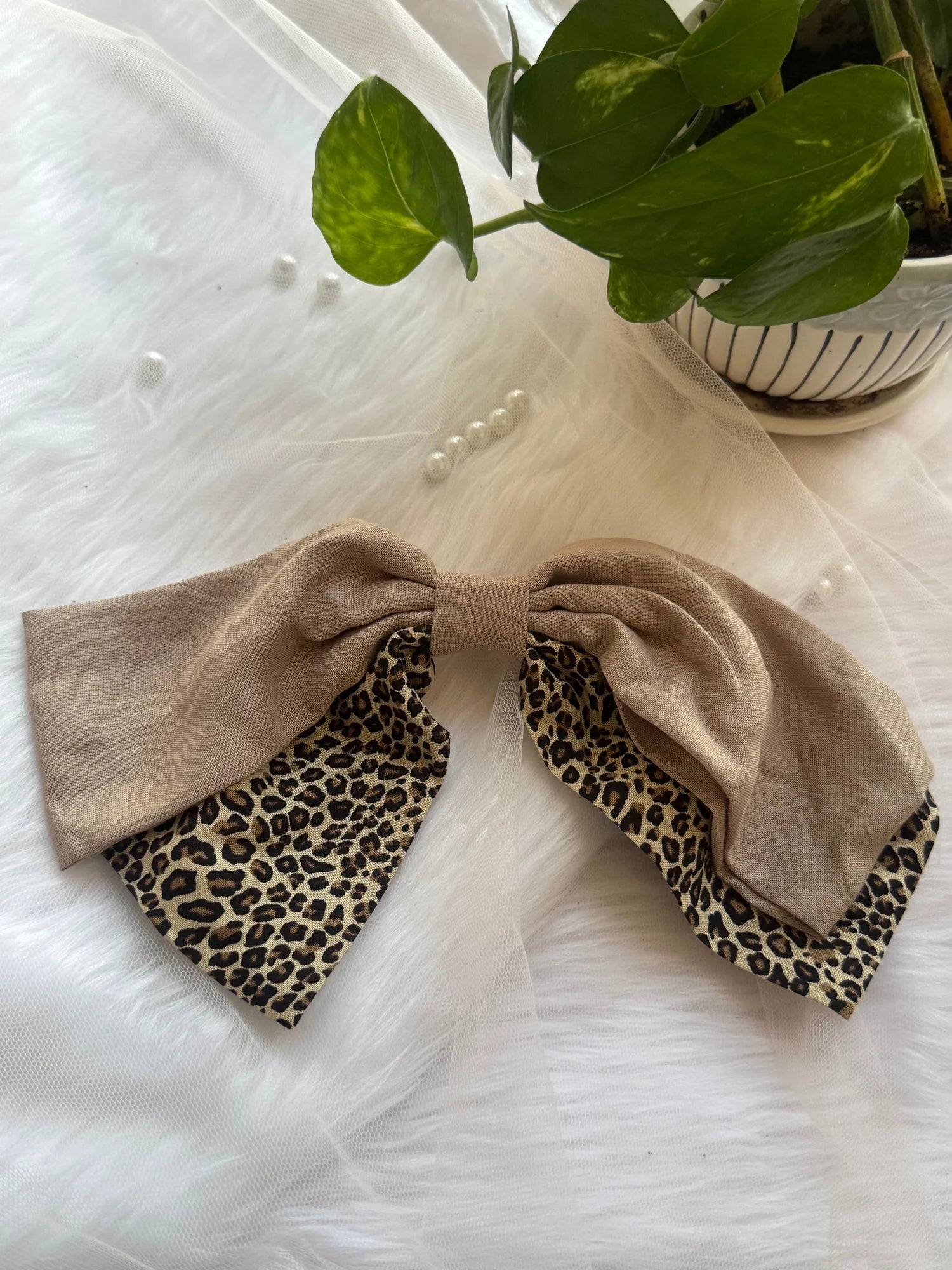 Beige and leopard print Madonna hair bow by Bows and Bags India displayed on white textured background with potted plant