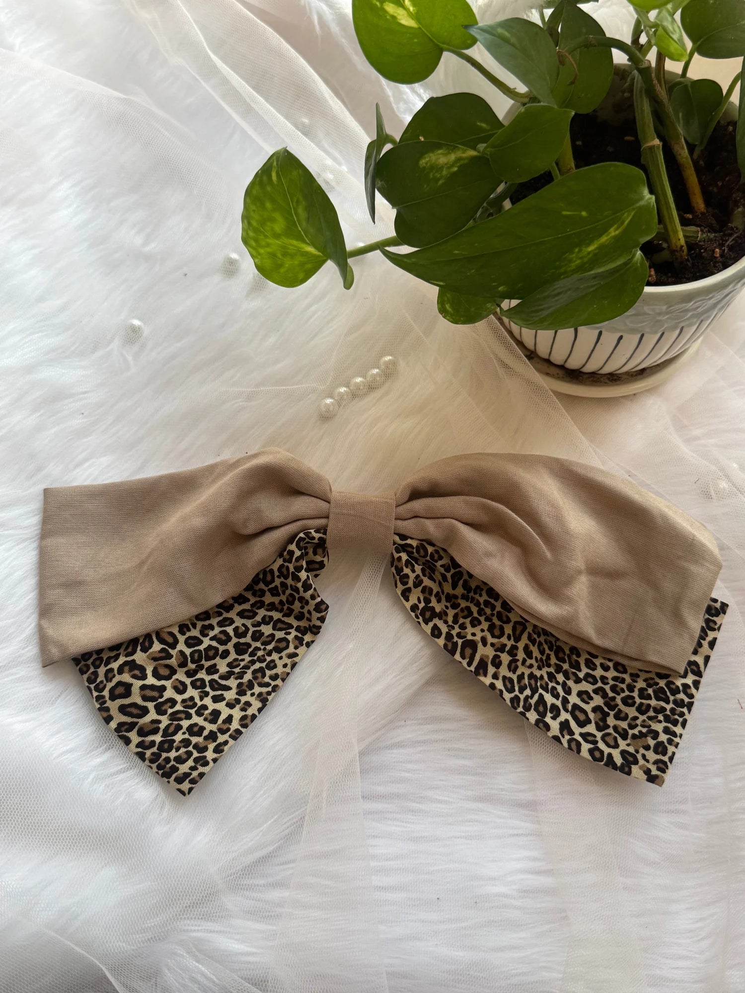 Beige and leopard print Madonna hair bow by Bows and Bags India displayed flat on white tulle with potted plant, showing