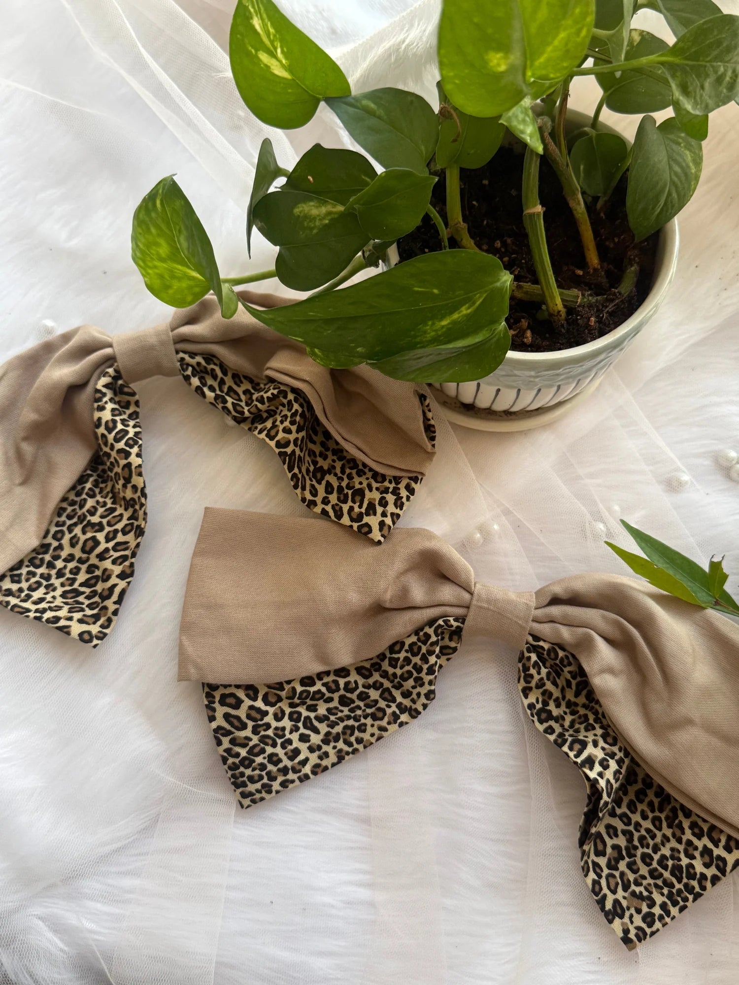 Beige and leopard print Madonna hair bow by Bows and Bags India displayed on white fabric with potted plant, showing