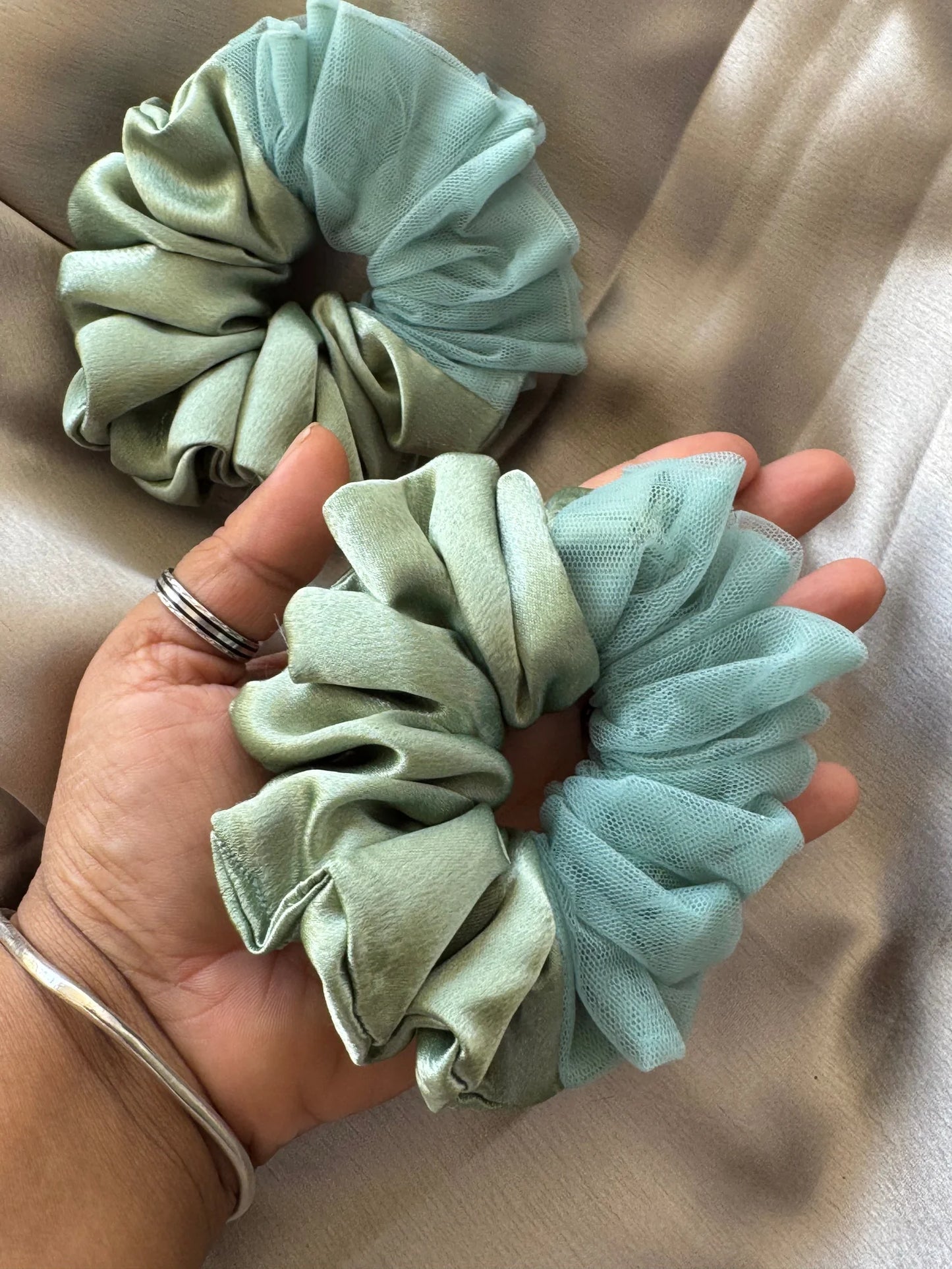 Metallic mint green satin and net scrunchie held in hand, showing luxe handmade texture and voluminous design by Bows and