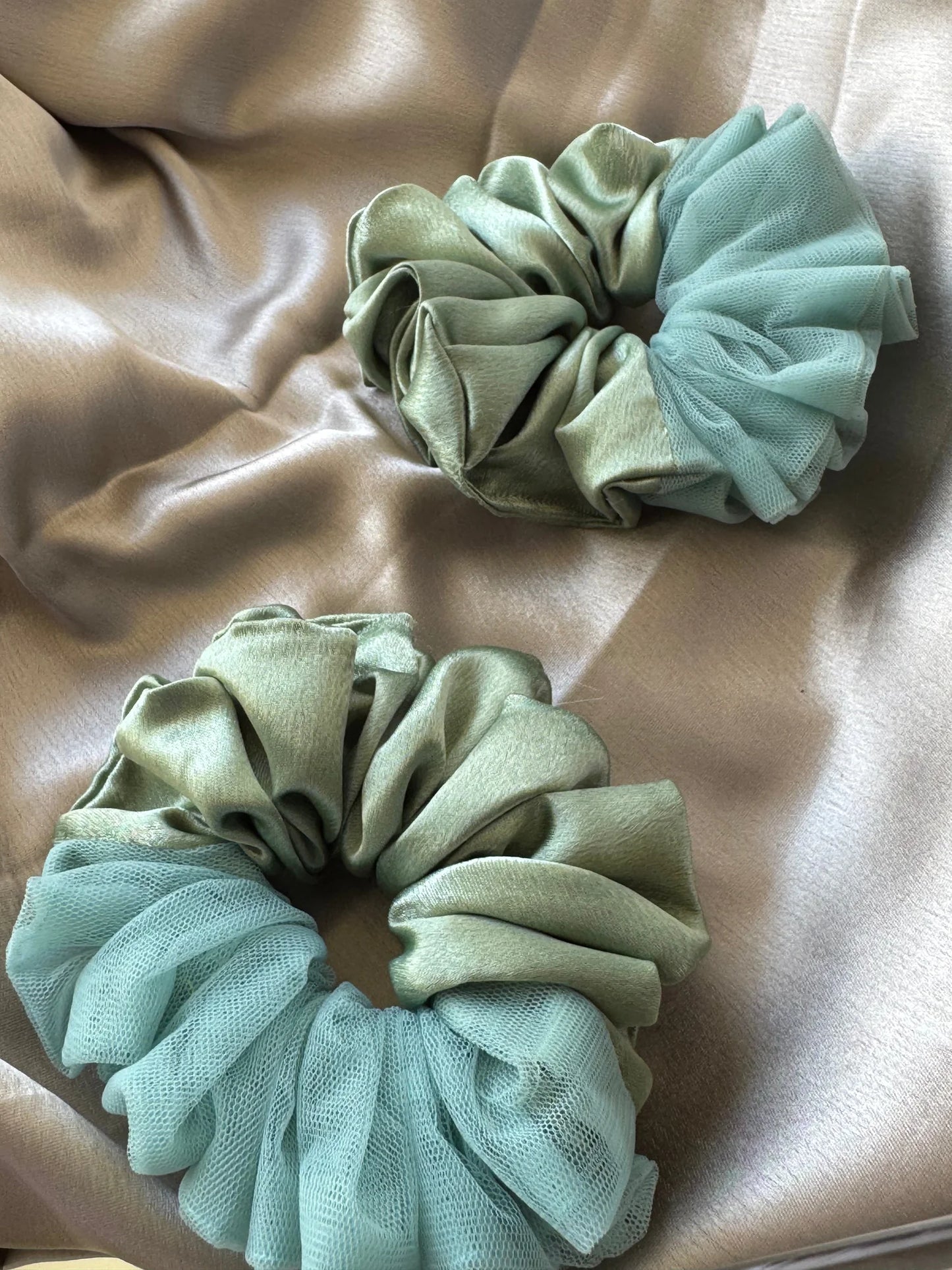Flat lay of two metallic mint green handmade satin scrunchies with delicate net borders by Bows and Bags India on neutral