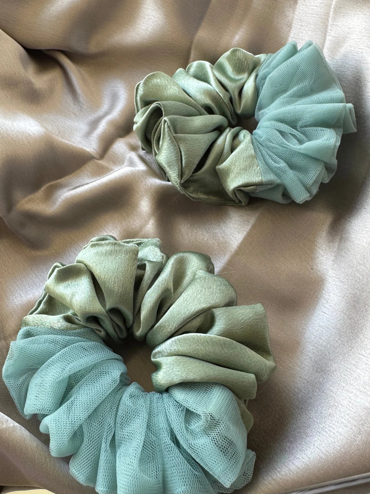 Flat lay of two metallic mint green handmade satin scrunchies with delicate net borders by Bows and Bags India on neutral