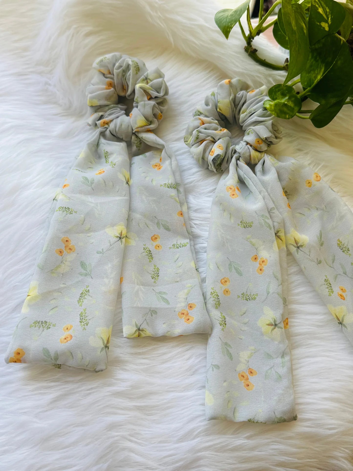 Light green floral georgette tail scrunchie with orange flowers by Bows and Bags India, displayed on white fur with flowing