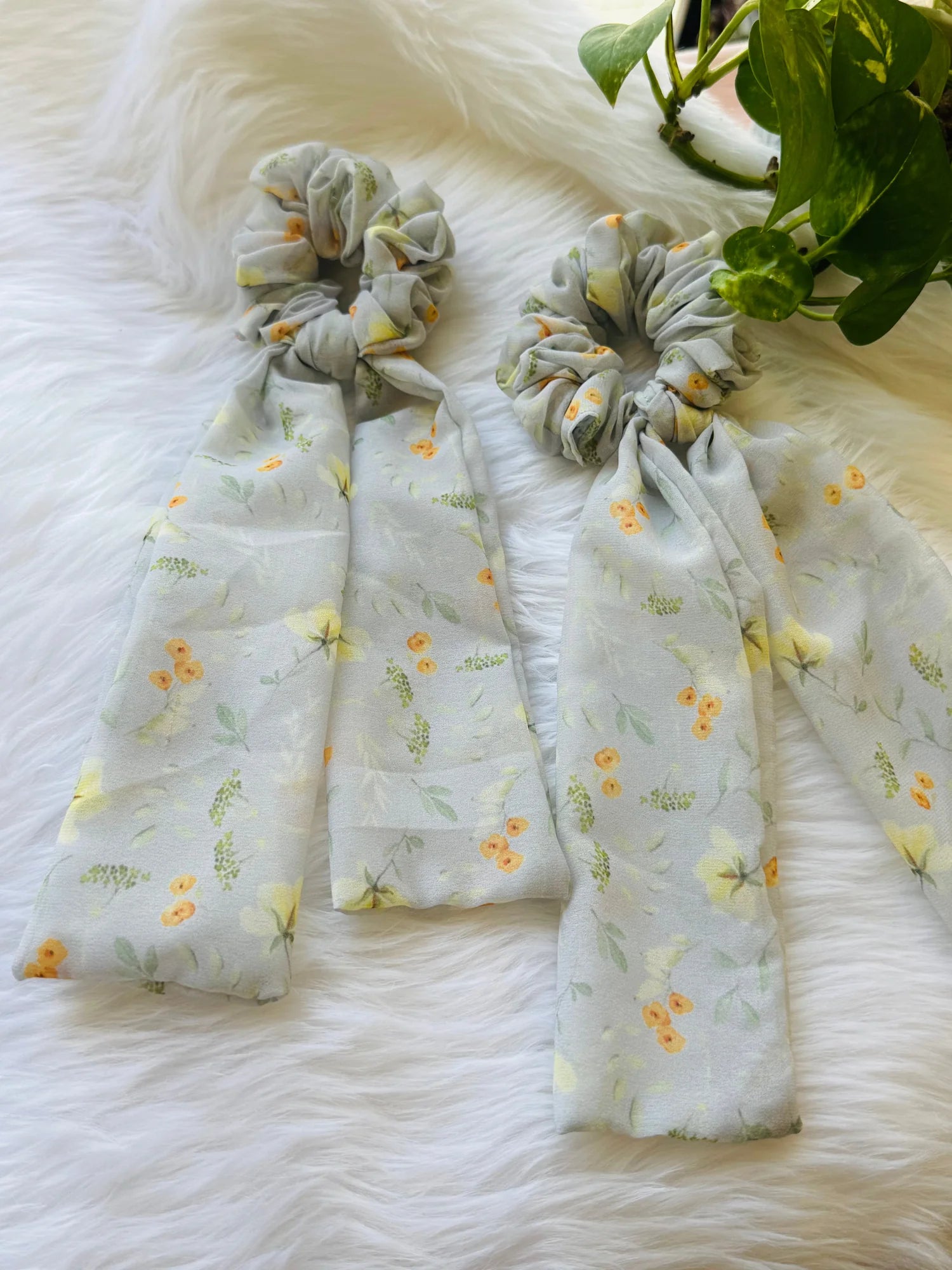 Light green floral georgette tail scrunchie with orange flowers by Bows and Bags India, displayed on white fur with flowing