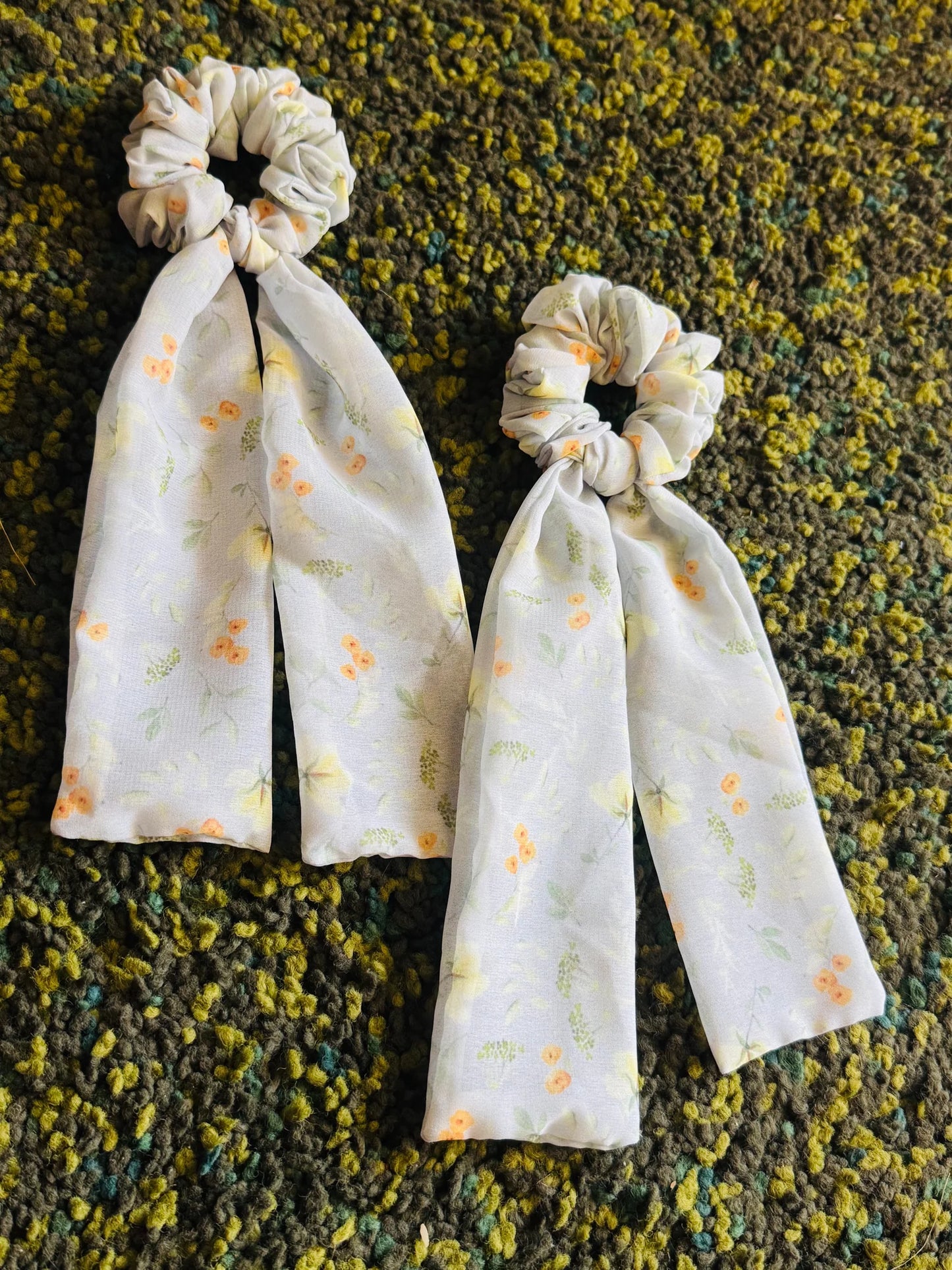 Two light green floral georgette tail scrunchies with flowing tails by Bows and Bags India, displayed on textured fabric