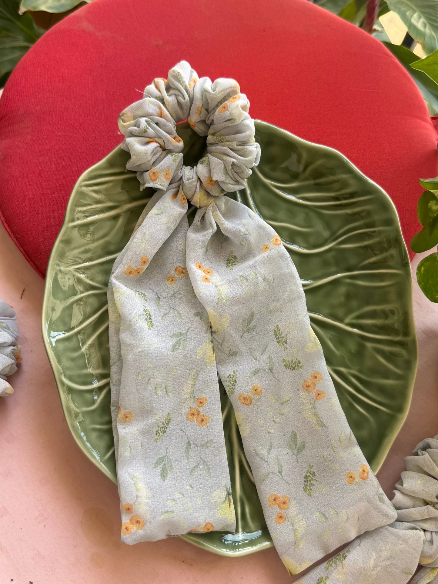 Light green floral georgette tail scrunchie by Bows and Bags India with flowing tails displayed on green velvet leaf,