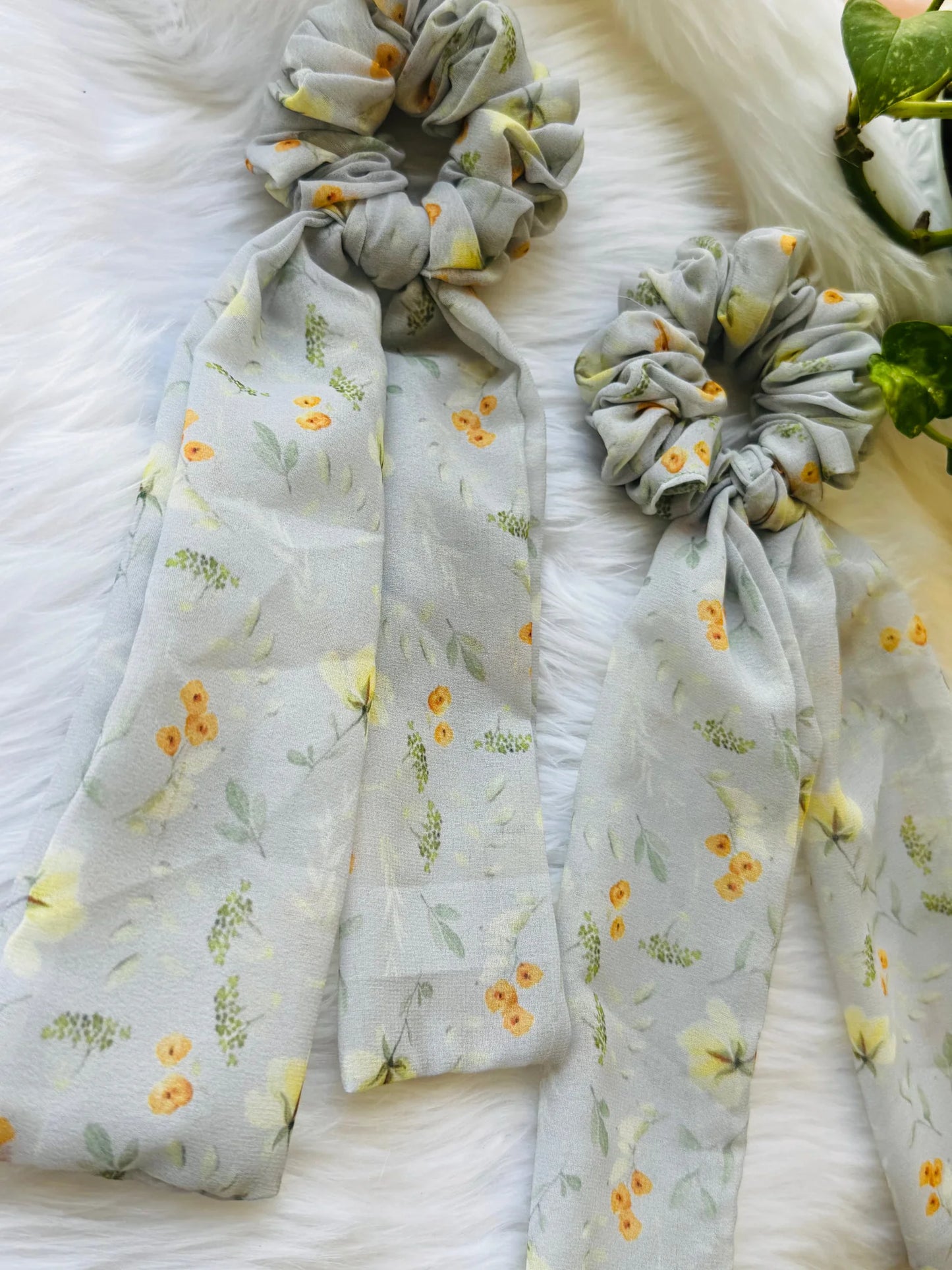 Floral green georgette tail scrunchie with yellow and orange flowers, displayed flat on white fur showing soft fabric