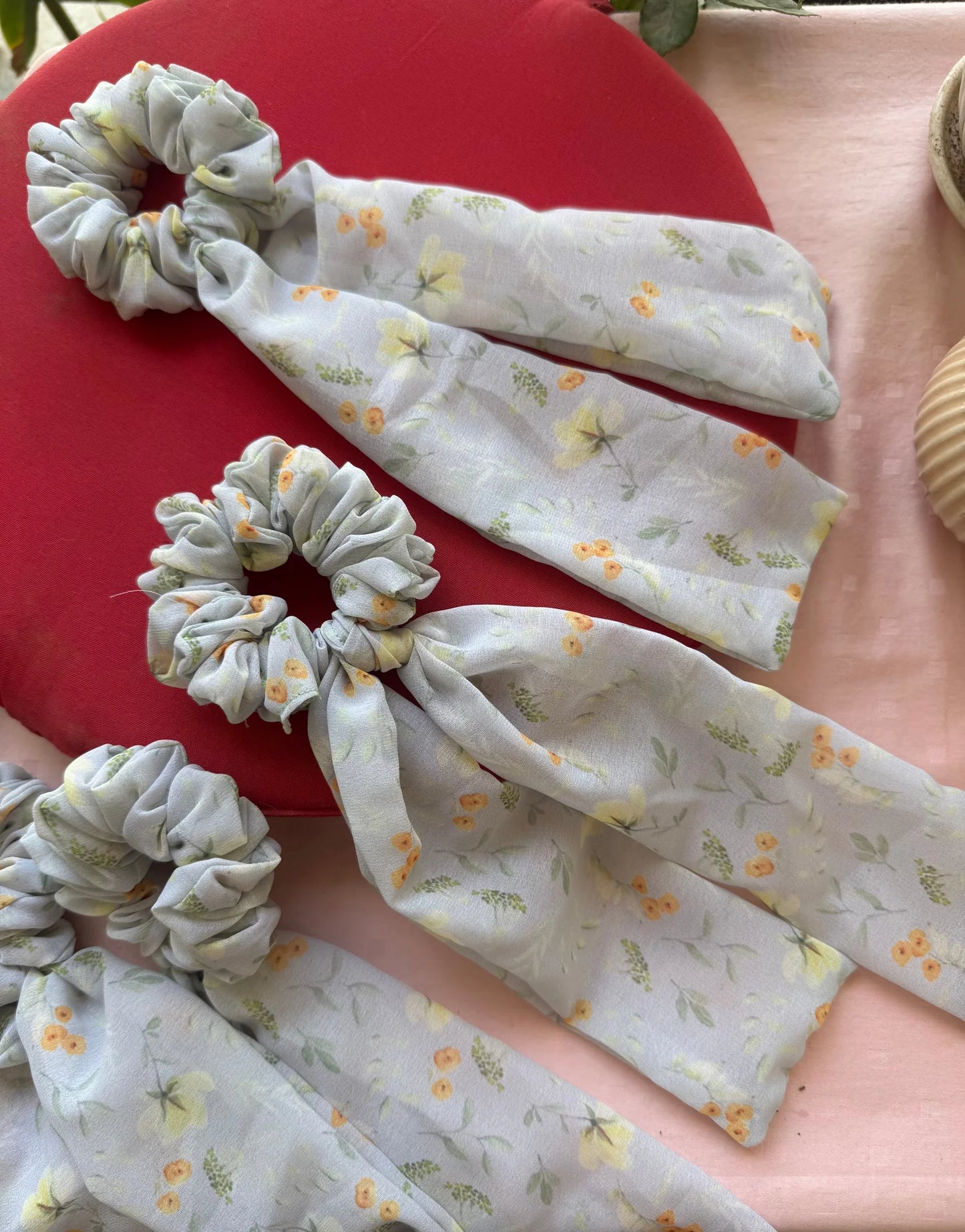 Three handmade floral georgette tail scrunchies by Bows and Bags India displayed on red and pink background, showing soft