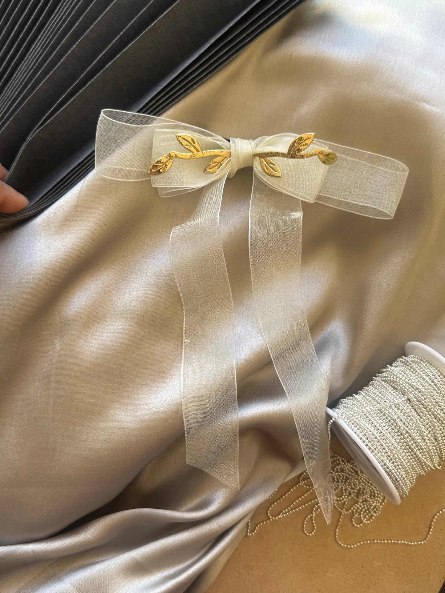 Transparent white organza bow hair clip with gold leaf accents from Bows and Bags India, handmade accessory displayed on