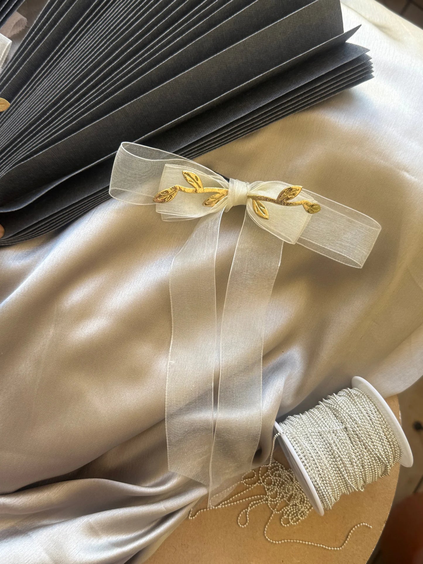 White transparent bow hair clip with gold leaf detailing by Bows and Bags India, displayed on cream silk fabric with styling