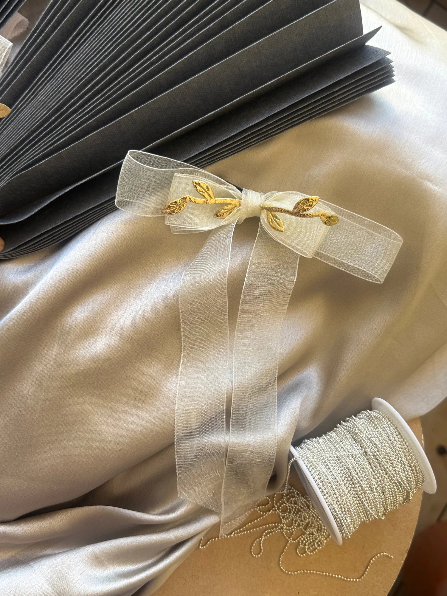 White transparent bow hair clip with gold leaf detailing by Bows and Bags India, displayed on cream silk fabric with styling