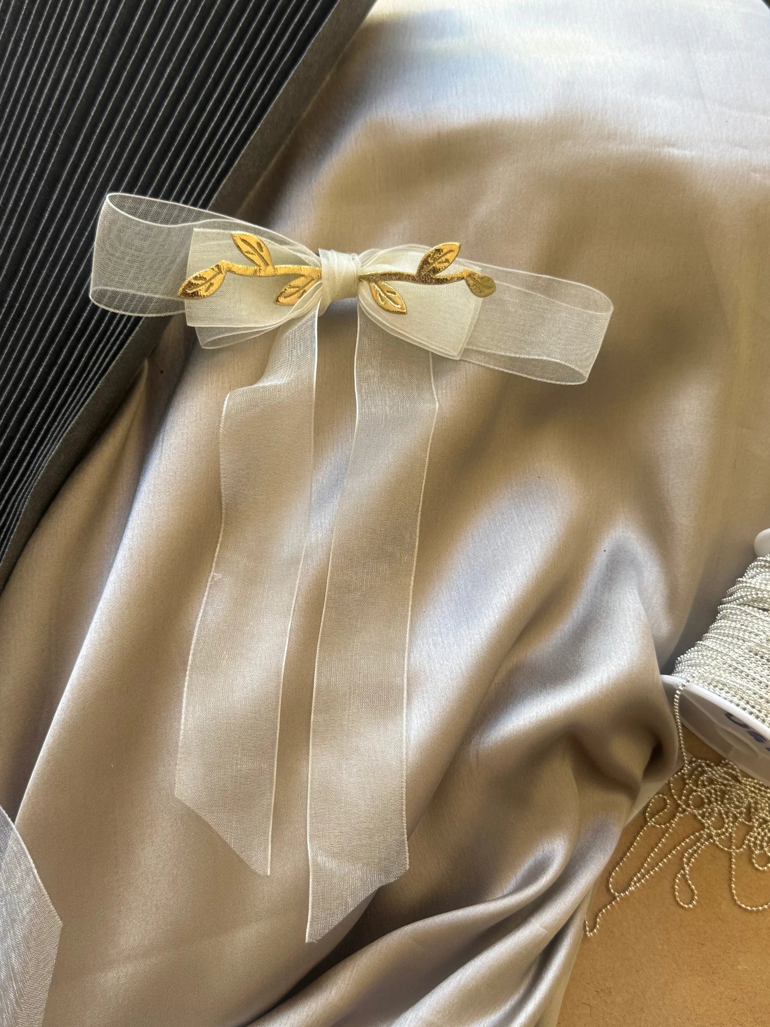 White transparent organza bow hair clip with gold leaf accents by Bows and Bags India, handmade accessory detail shot