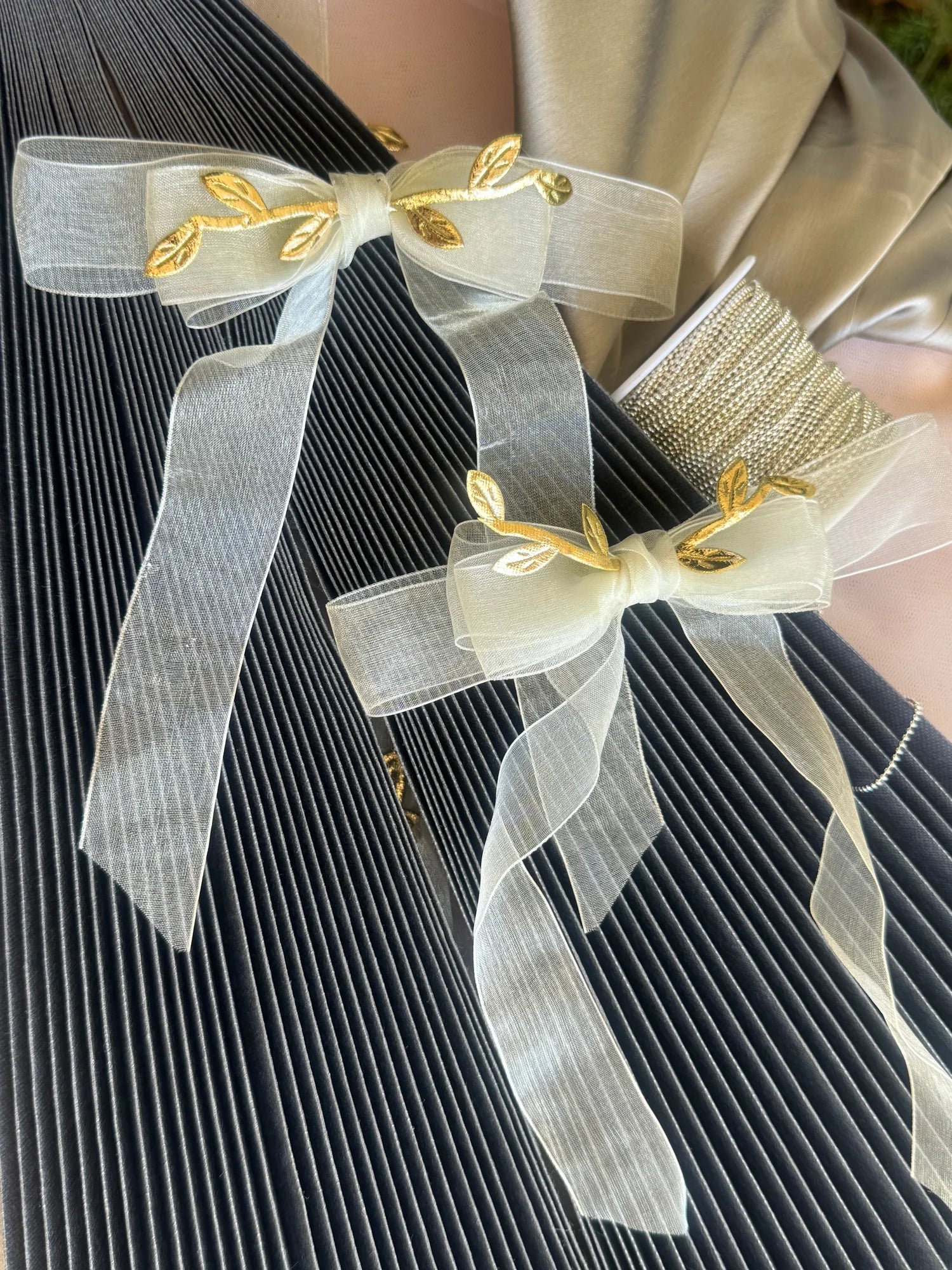 Close-up of white transparent bow hair clip with gold leaf details on dark pleated fabric, lifestyle shot by Bows and Bags