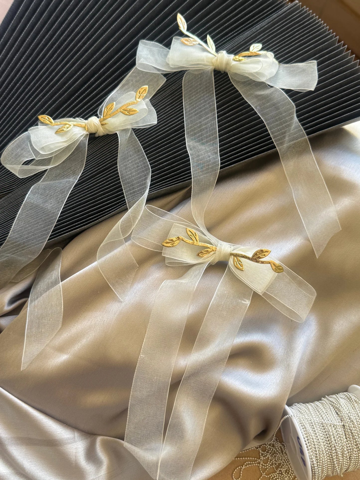 White transparent bow hair clip with gold leaf detailing by Bows and Bags India, handmade accessory on cream fabric