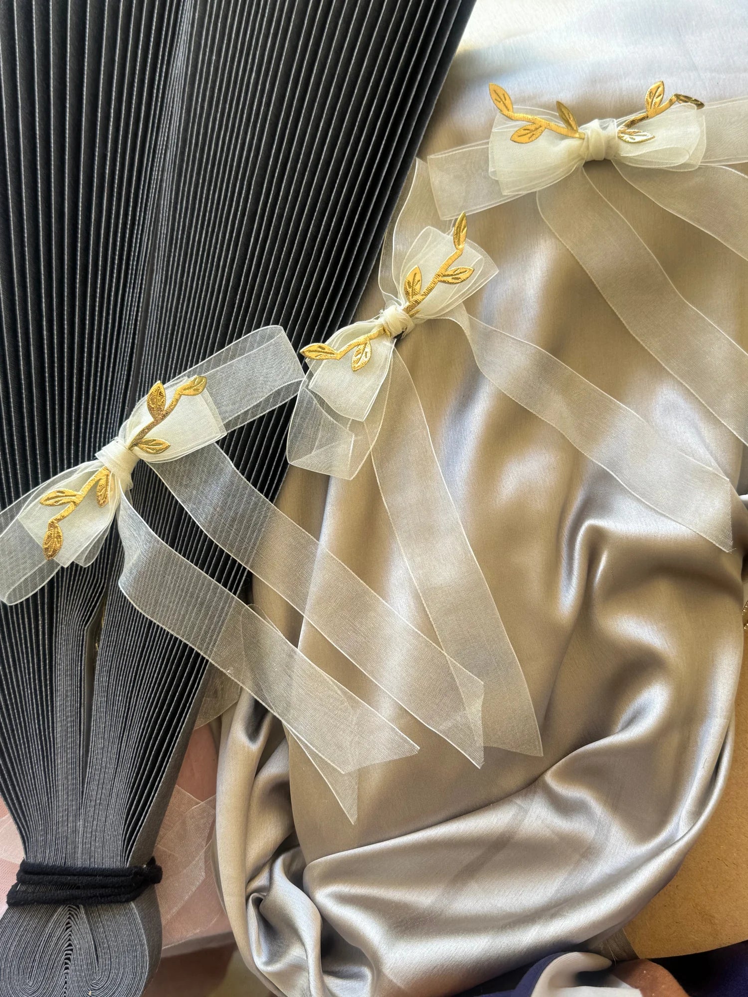White transparent bow hair clip with gold leaf details by Bows and Bags India, elegant handmade accessory styled on grey