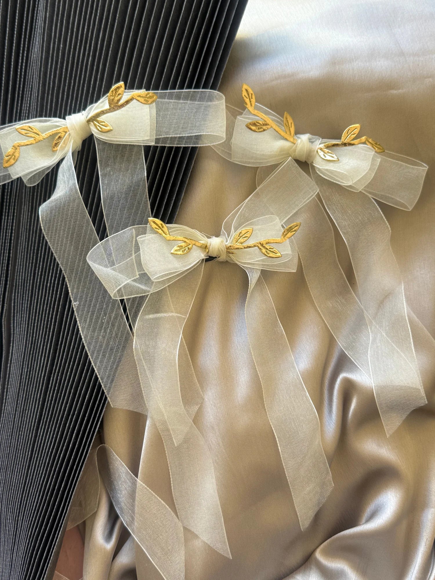 White transparent bow hair clip with gold leaf details by Bows and Bags India, elegant handmade accessory displayed on cream