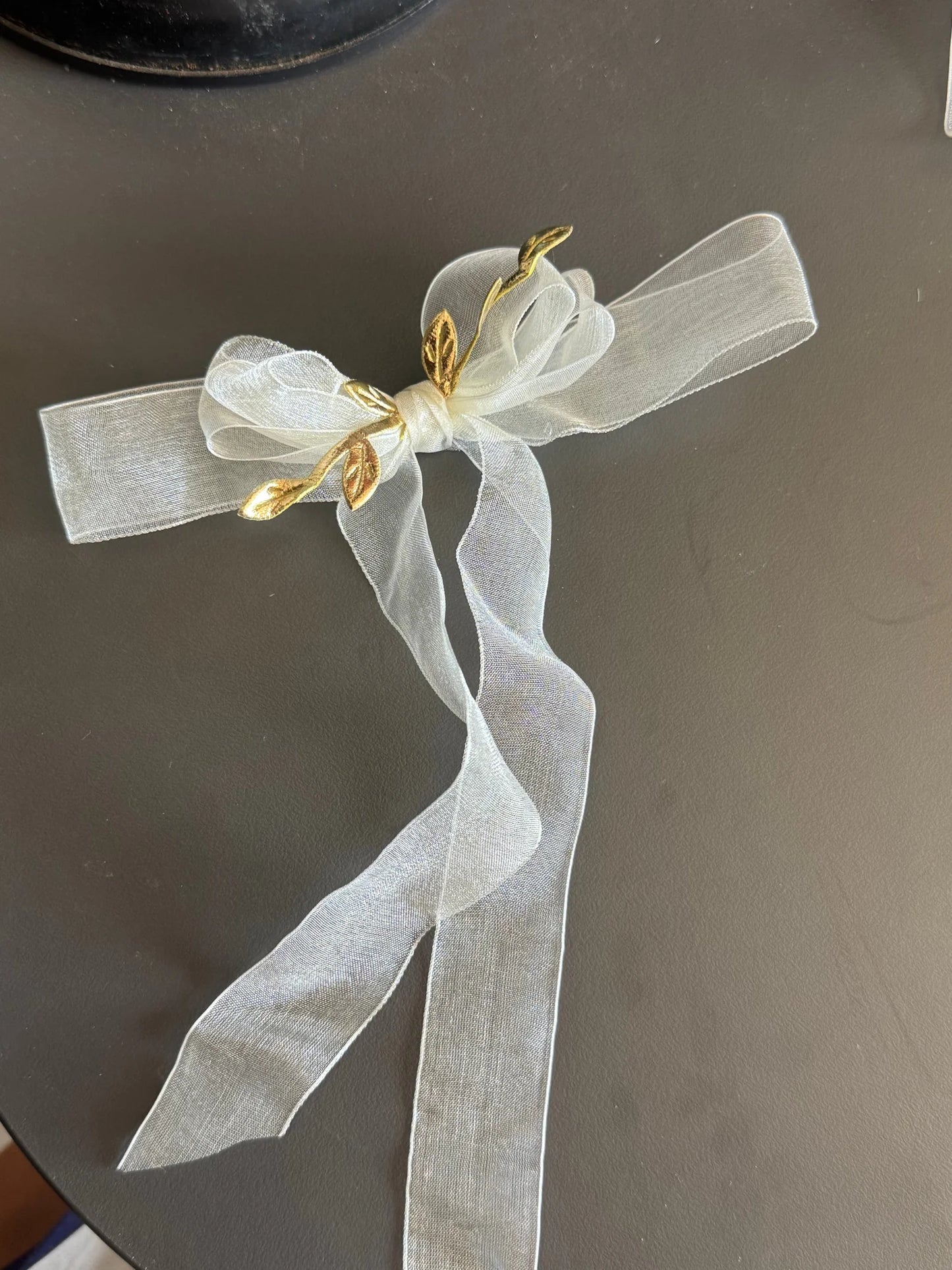 White transparent bow hair clip with gold leaf details by Bows and Bags India, elegant handmade accessory displayed flat lay