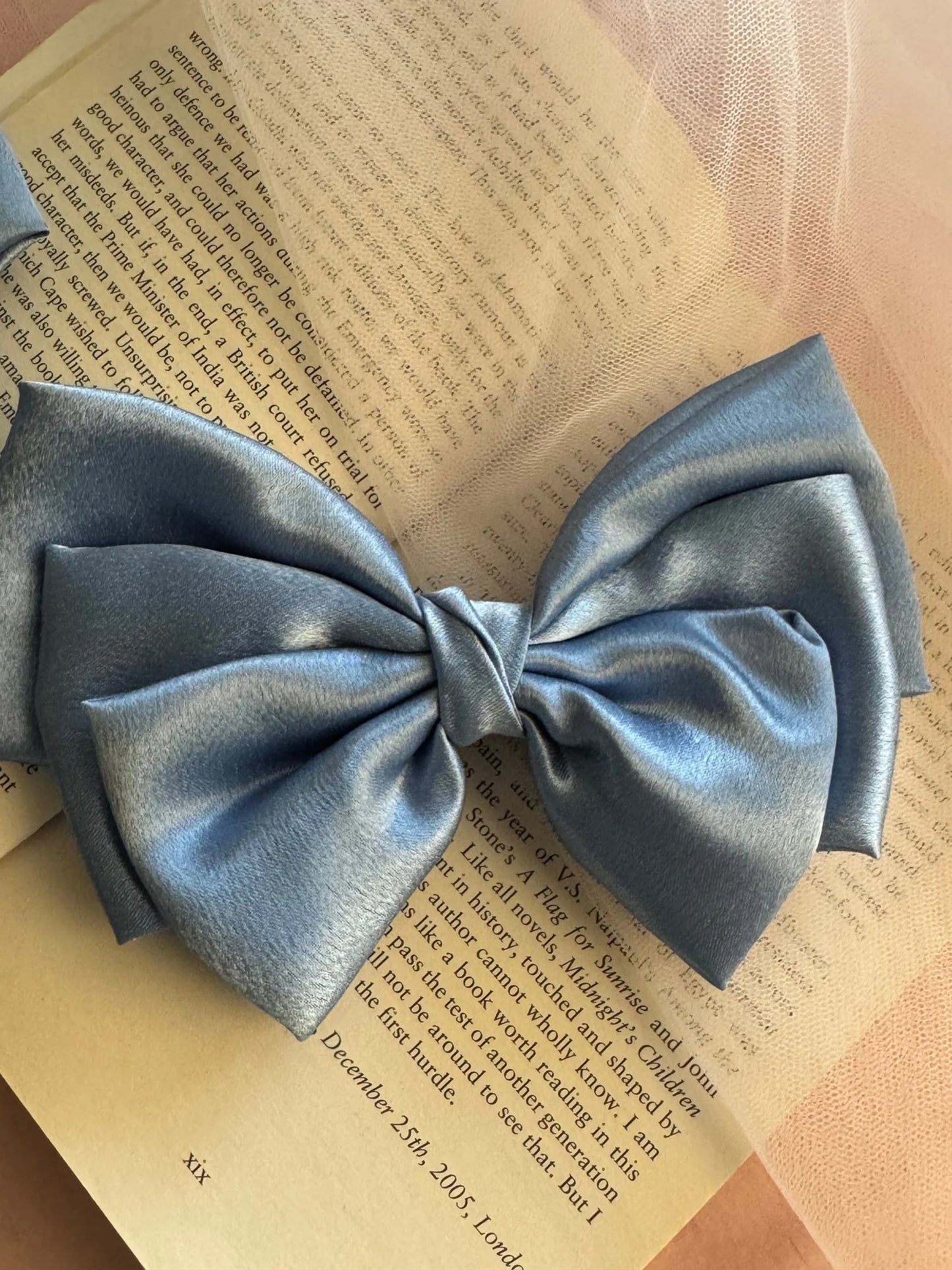 Metallic ice blue satin hair bow by Bows and Bags India displayed on open book, showcasing luxe handmade texture and elegant