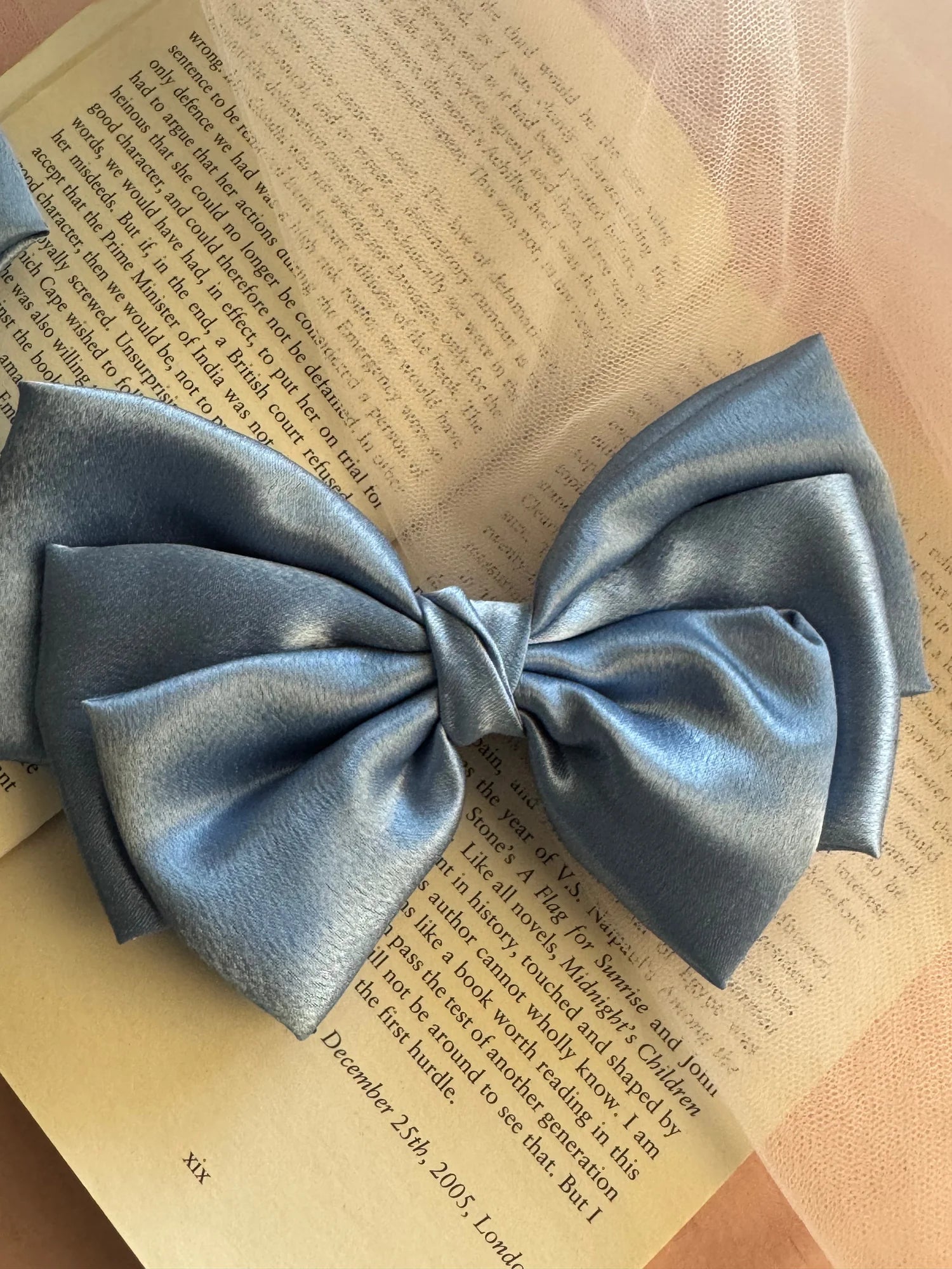 Metallic ice blue satin hair bow by Bows and Bags India displayed on open book, showcasing luxe handmade texture and elegant