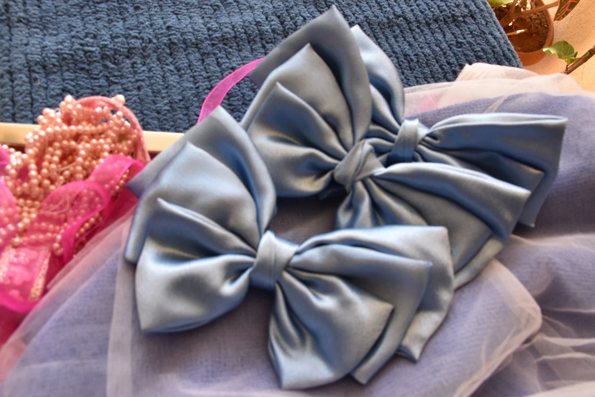 Metallic ice blue satin hair bows displayed on lavender fabric, handmade accessory collection by Bows and Bags India