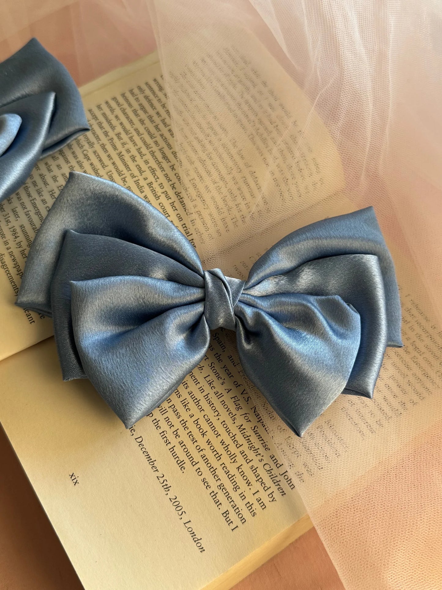 Metallic ice blue satin hair bow by Bows and Bags India displayed on open book, showcasing elegant handmade bow texture and