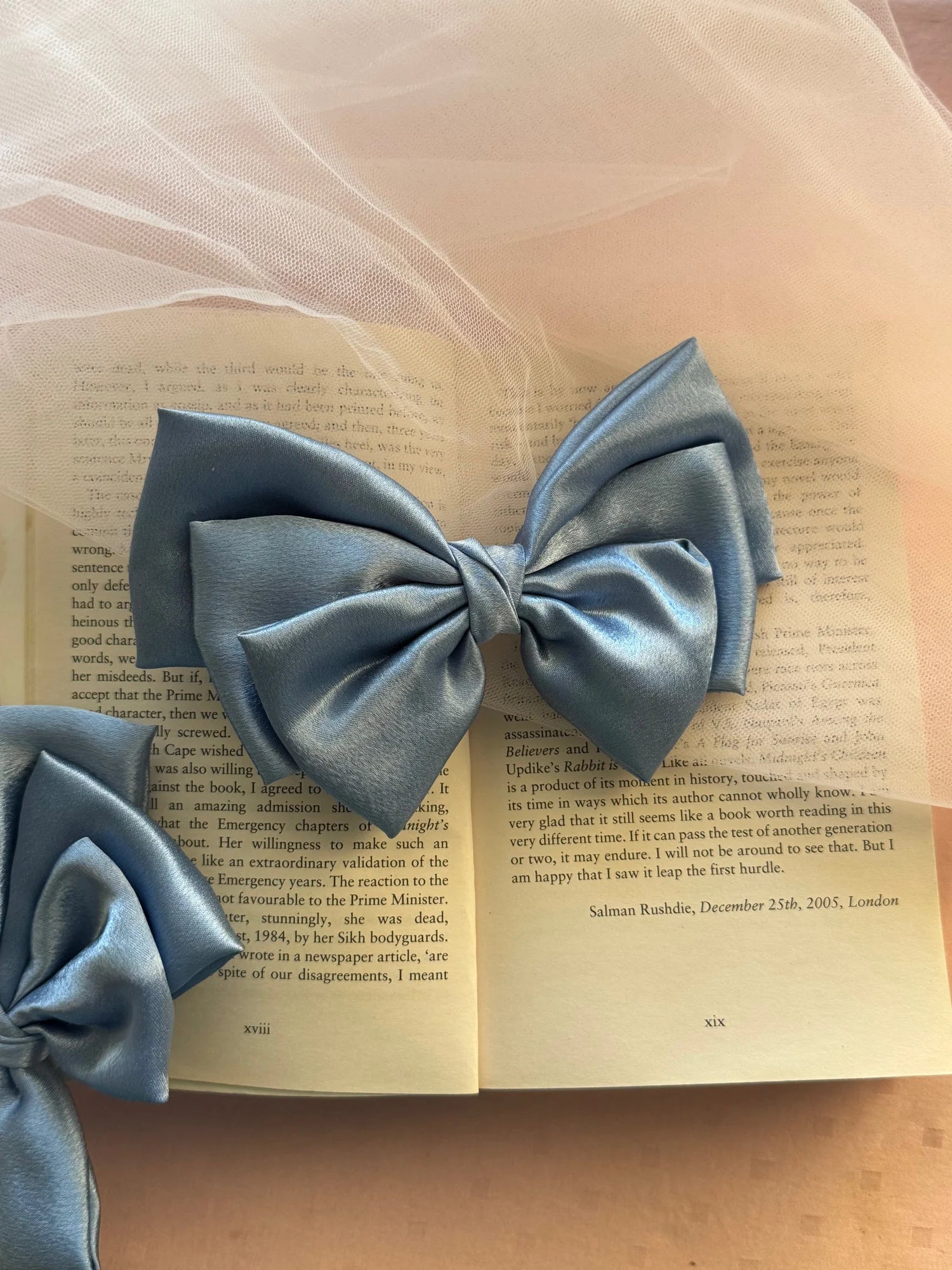 Metallic ice blue satin hair bow from Bows and Bags India displayed on open book pages, lifestyle shot