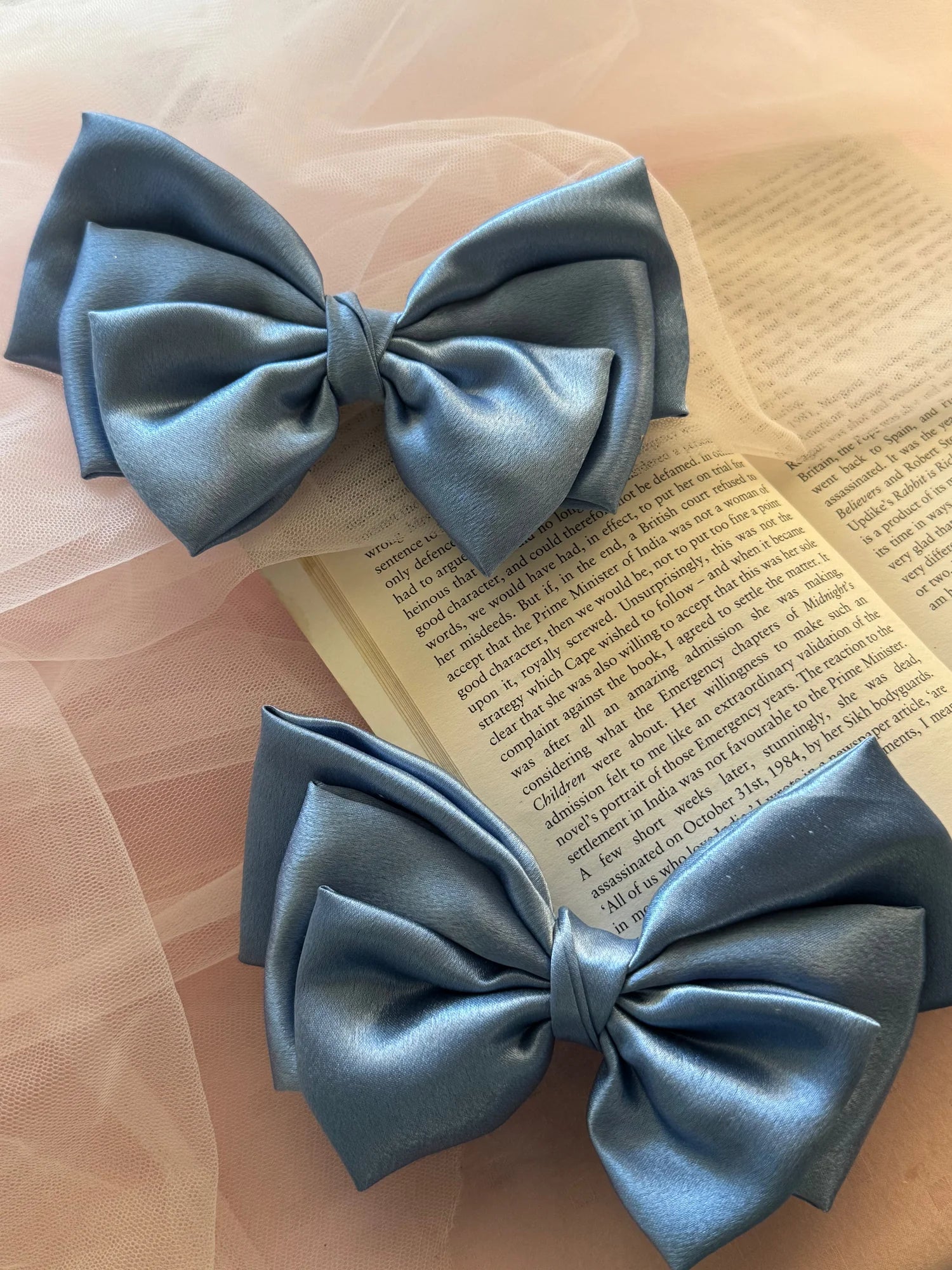Metallic ice blue satin hair bows displayed on open book, handmade accessories by Bows and Bags India showing elegant