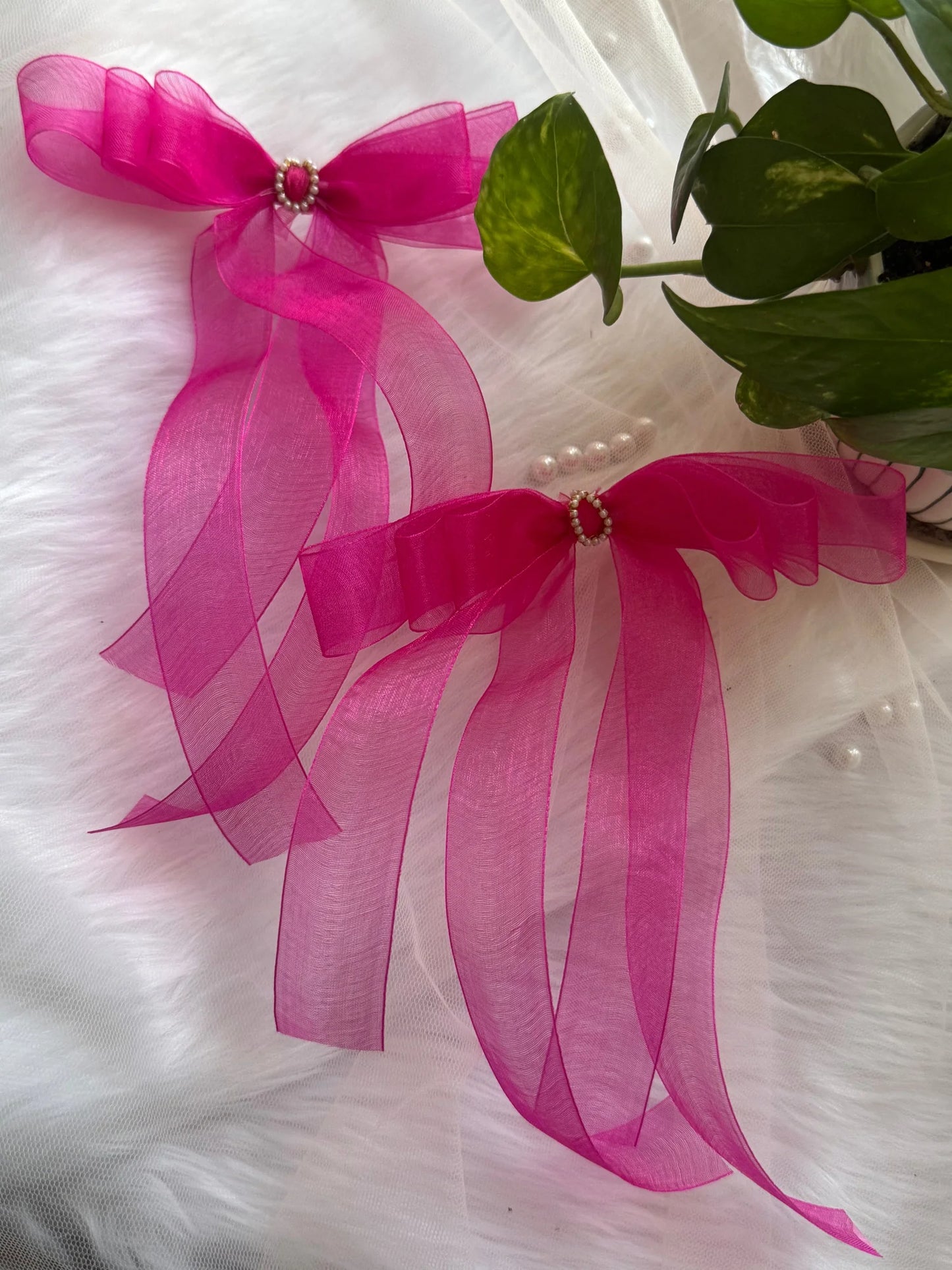 Pink organza hair bow with pearl center detail by Bows and Bags India, displayed on white fabric with green foliage