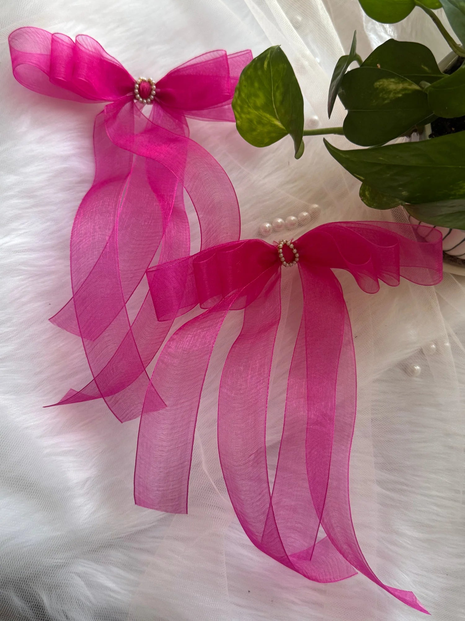 Pink organza hair bow with pearl center detail by Bows and Bags India, displayed on white fabric with green foliage