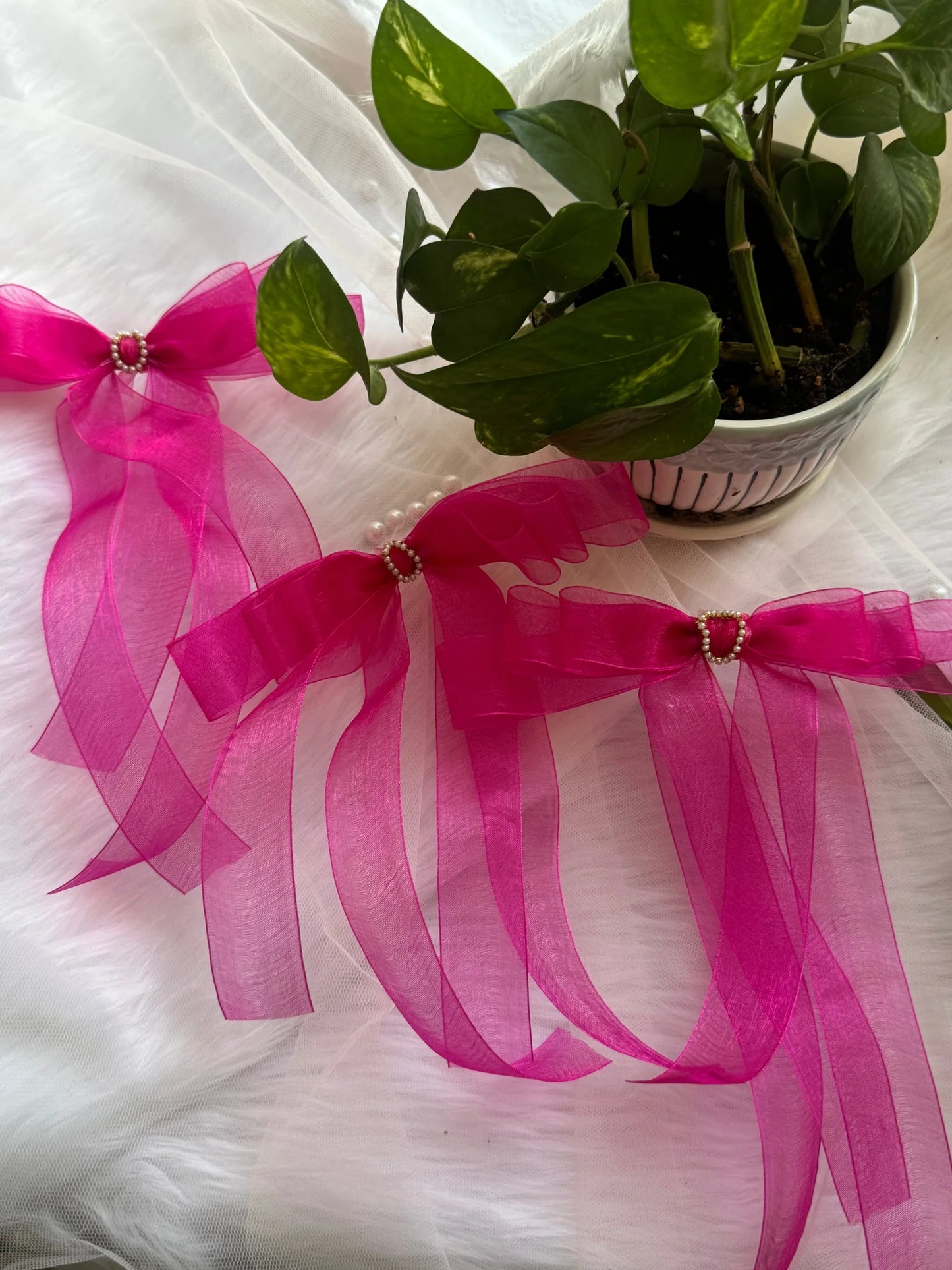 Pink Crush organza hair bow with pearl detail by Bows and Bags India, displayed with potted green plant on white fabric
