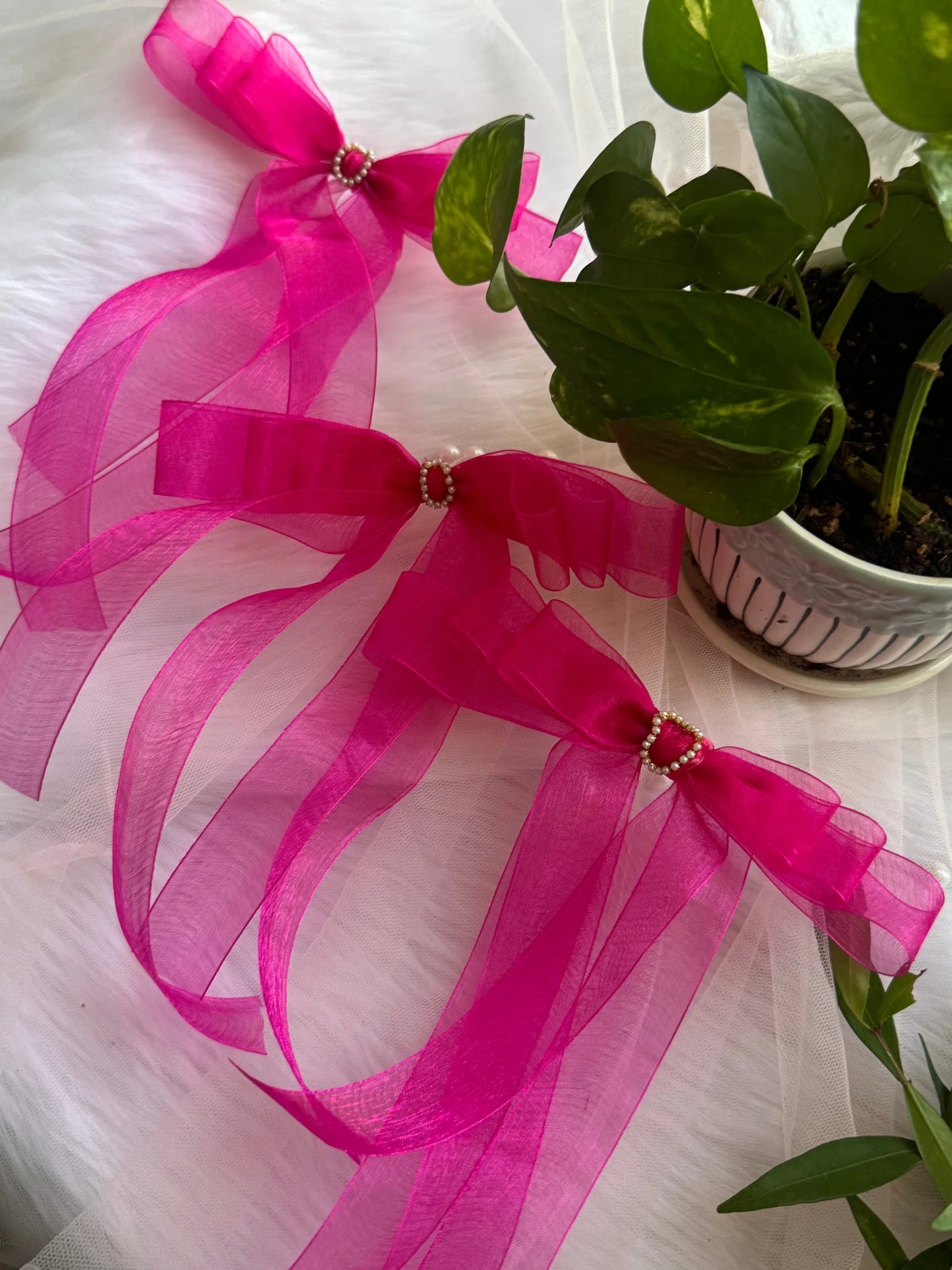 Hot pink organza hair bow with pearl detailing by Bows and Bags India, displayed with green plant styling