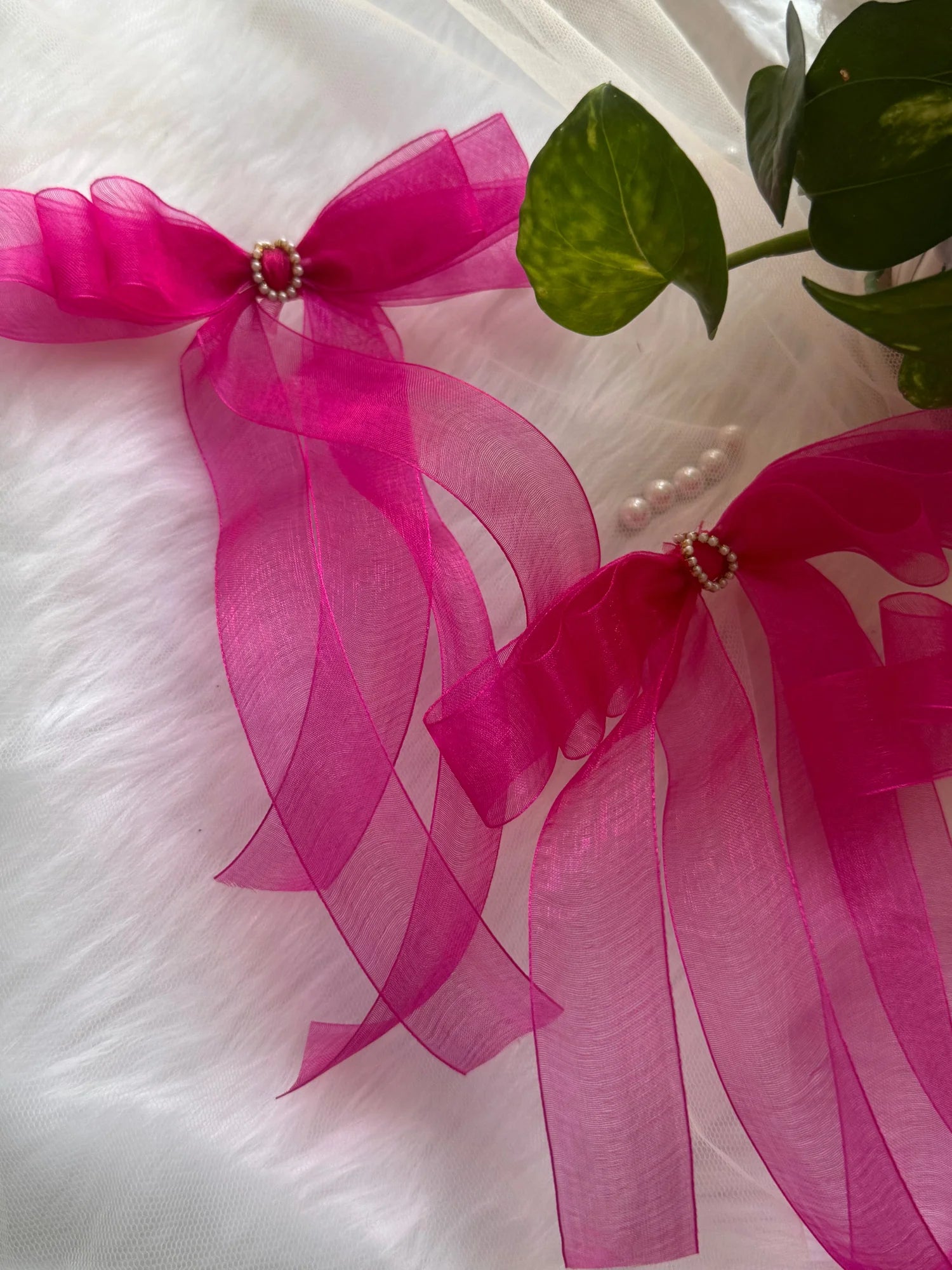 Pink organza hair bow with pearl detail and green leaves, handmade hair accessory by Bows and Bags India on white fabric