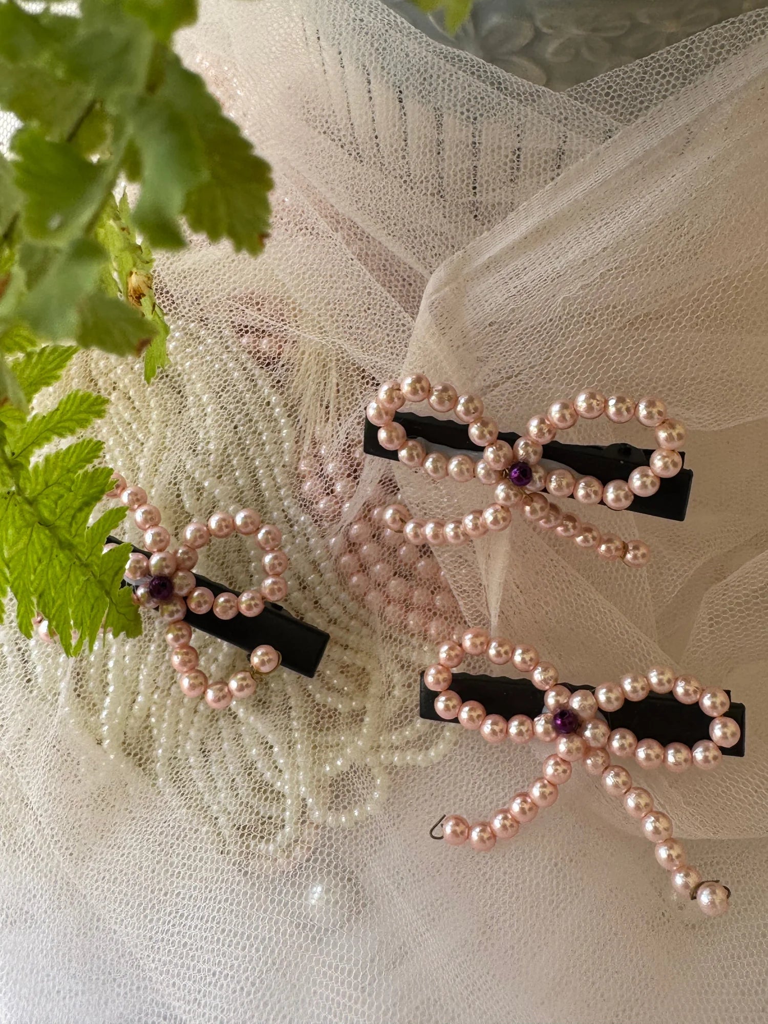Pink pearl bow hair clip with delicate pearl strings displayed on cream tulle fabric by Bows and Bags India handmade