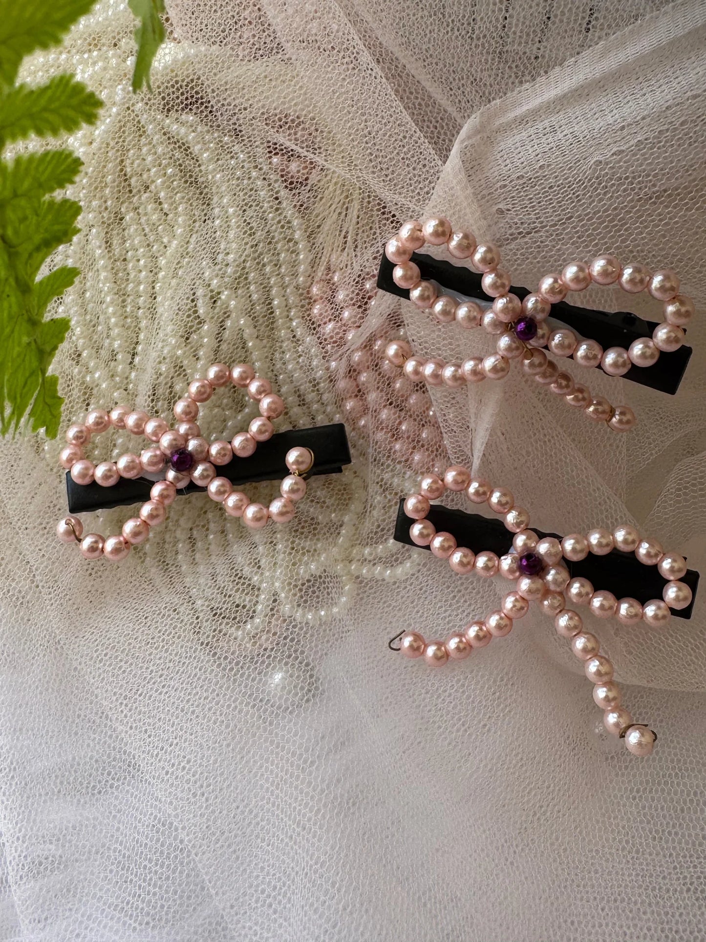 Pink pearl bow hair clips with black bases displayed on cream lace fabric by Bows and Bags India handmade hair accessories