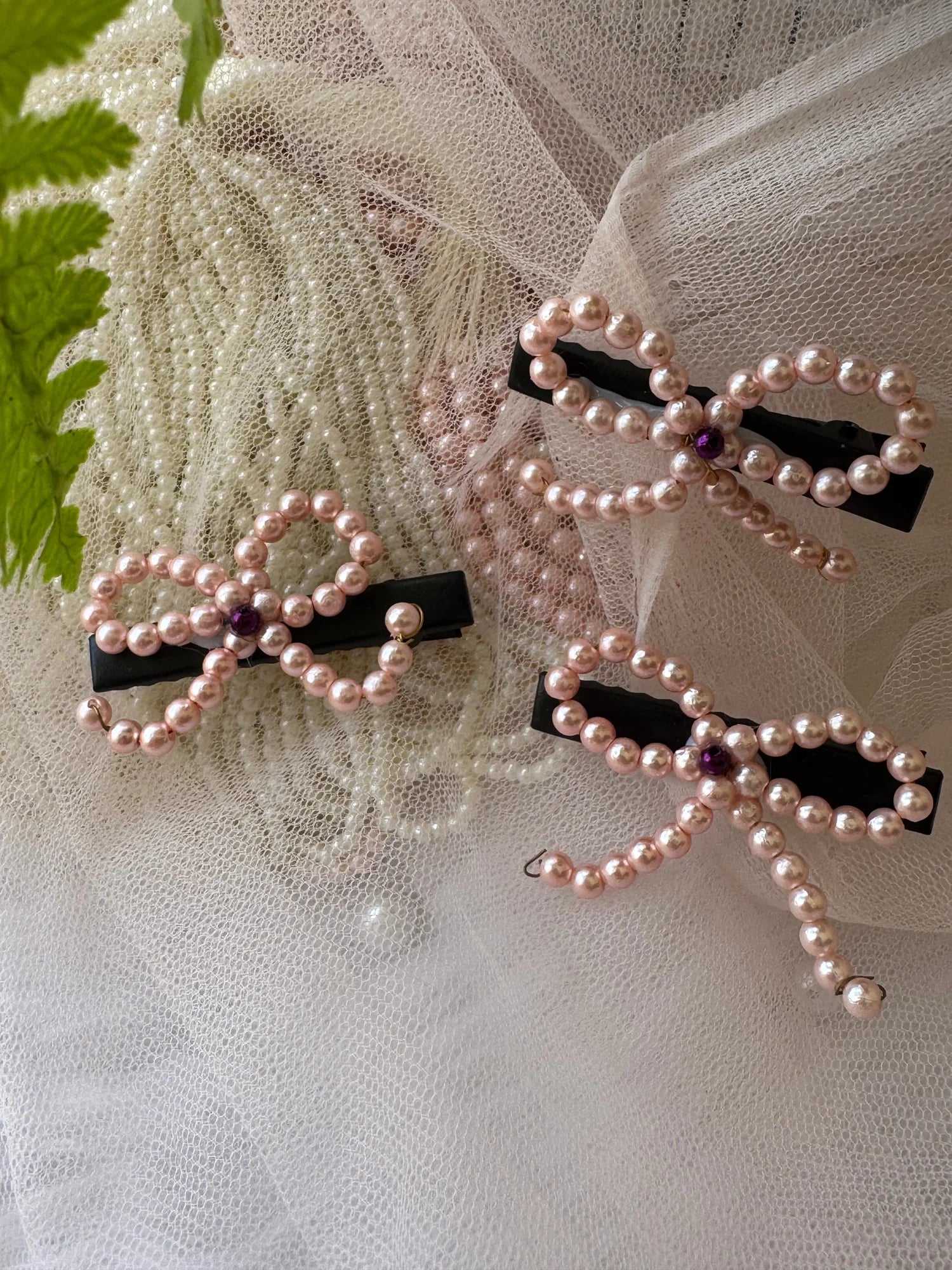 Pink pearl bow hair clips with black bases displayed on cream lace fabric by Bows and Bags India handmade hair accessories