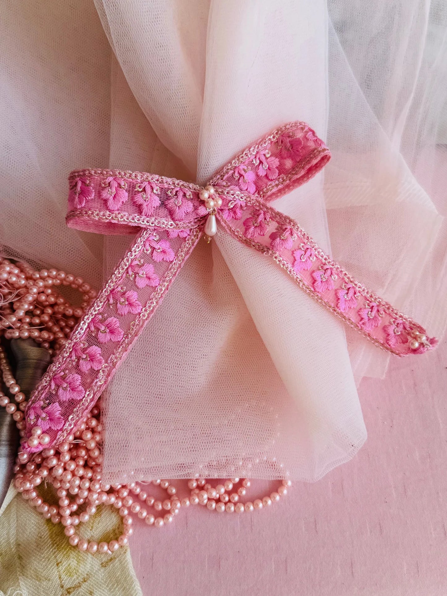 Pink pearl flower hair clip with embroidered floral details and pearl center by Bows and Bags India, displayed on tulle