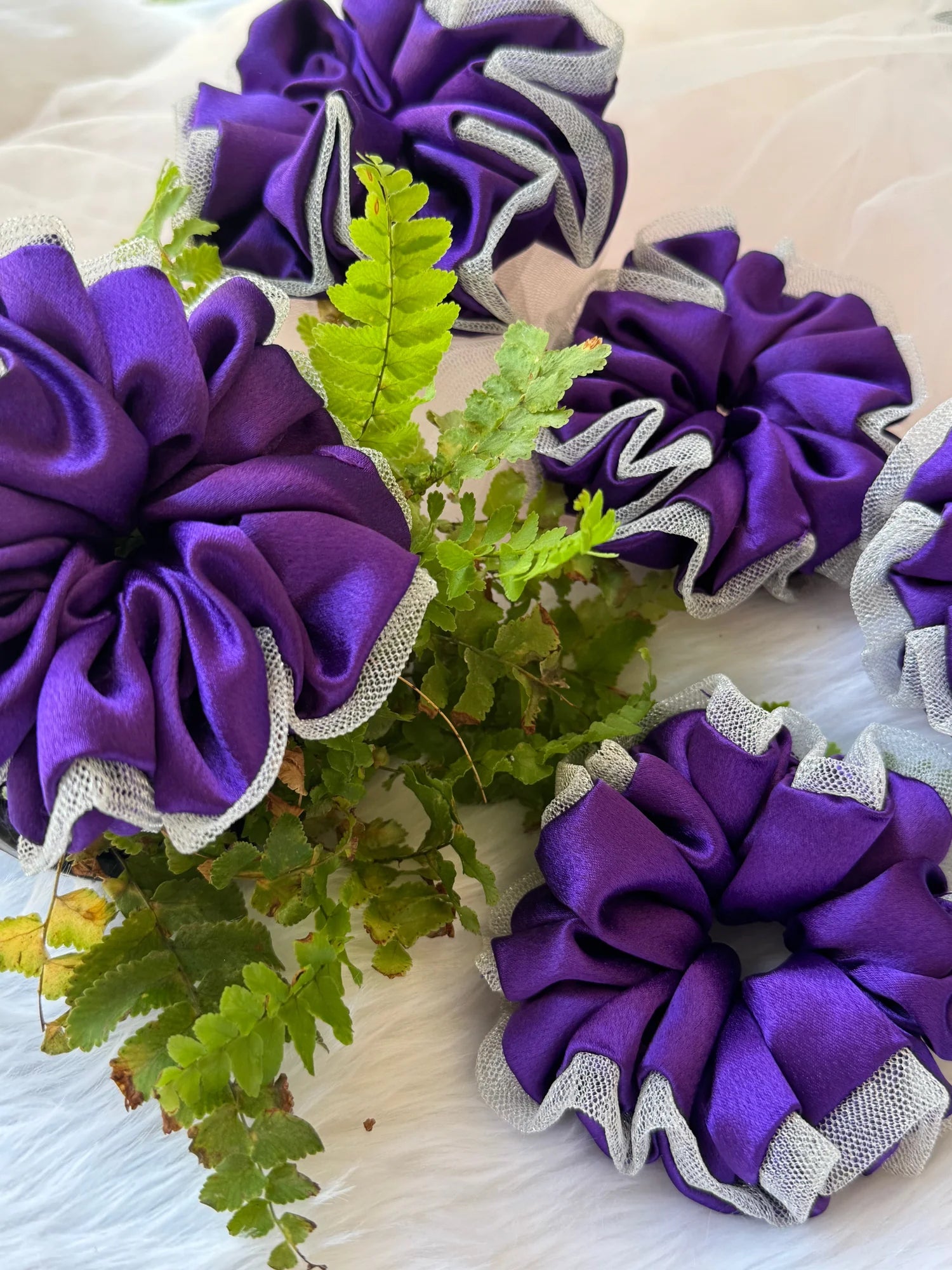Purple satin scrunchie with silver net border, handmade hair accessory by Bows and Bags India, displayed with green foliage