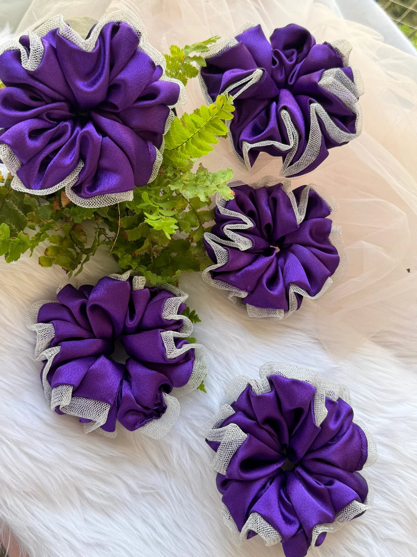 Five purple satin scrunchies with silver net borders arranged on white fur, handmade hair accessories by Bows and Bags India