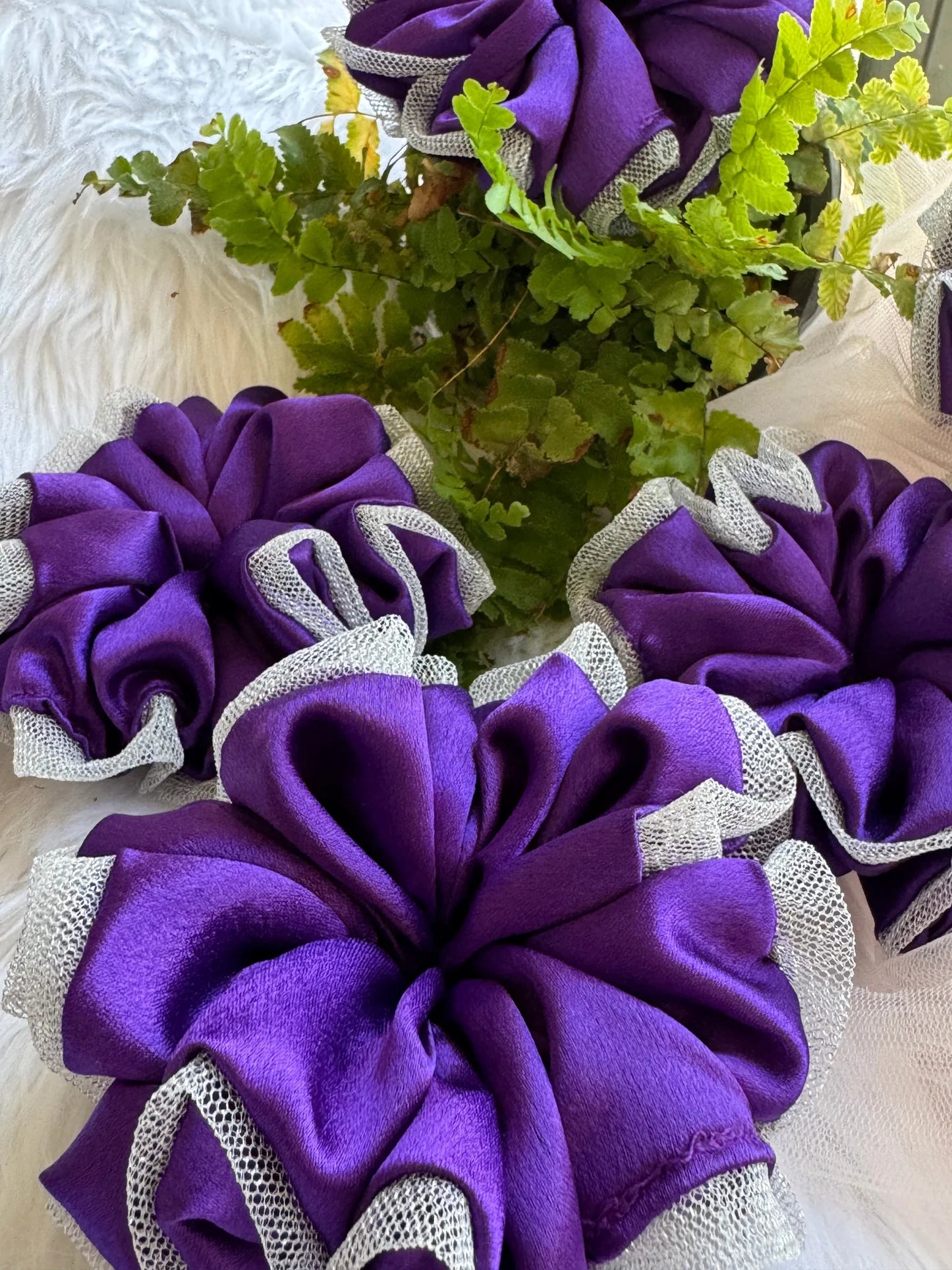Purple satin scrunchie with silver net border by Bows and Bags India, handmade hair accessory displayed with green foliage