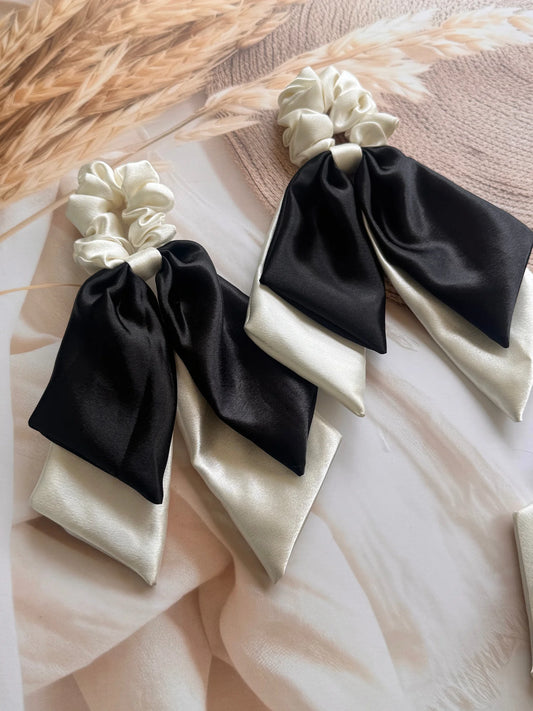 Pearly white and black satin dual long tail scrunchies with bow detail by Bows and Bags India, displayed on neutral fabric