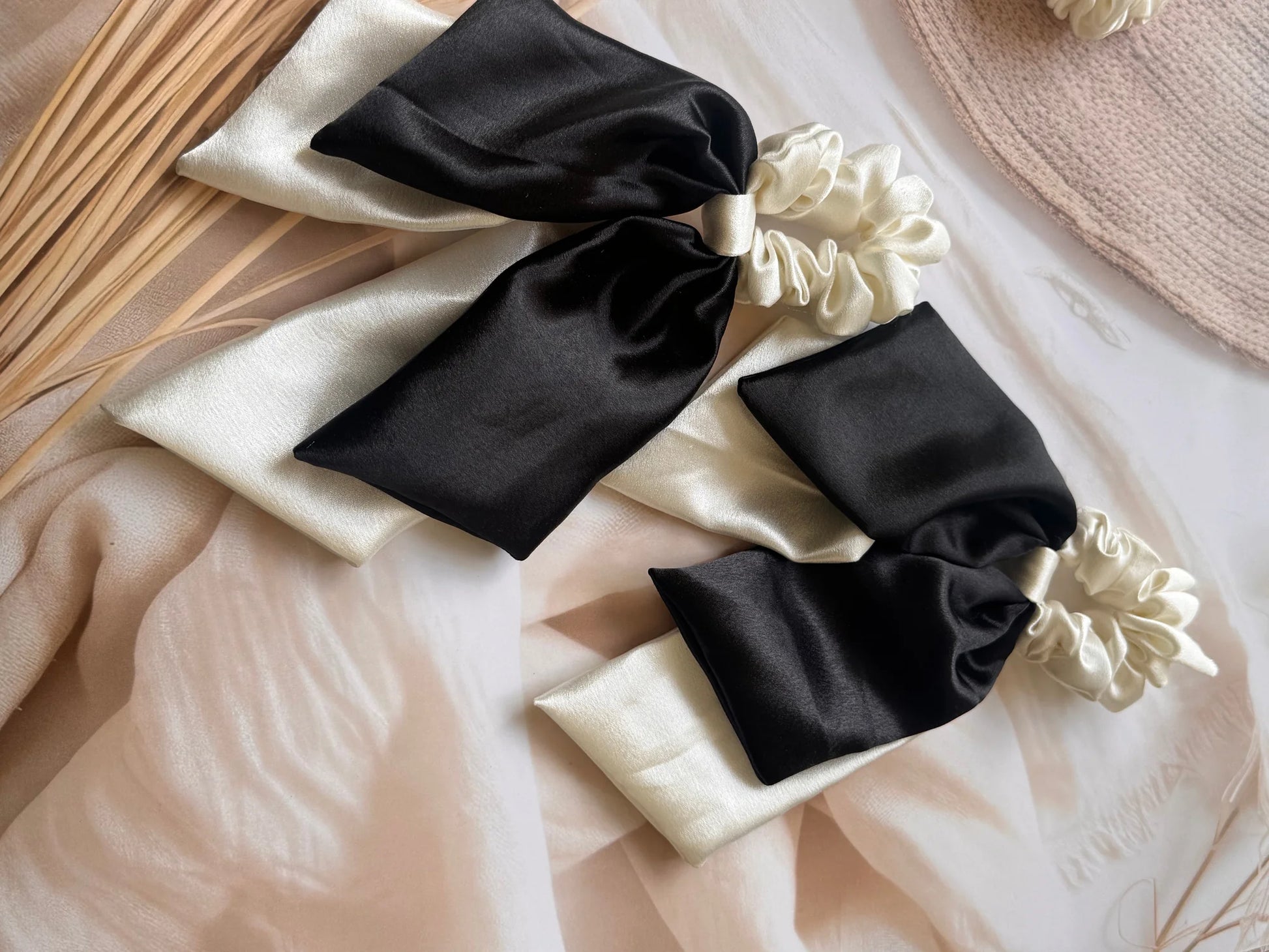 Bows and Bags India handmade satin dual long tail scrunchies in black and cream, styled flat lay with dried florals and