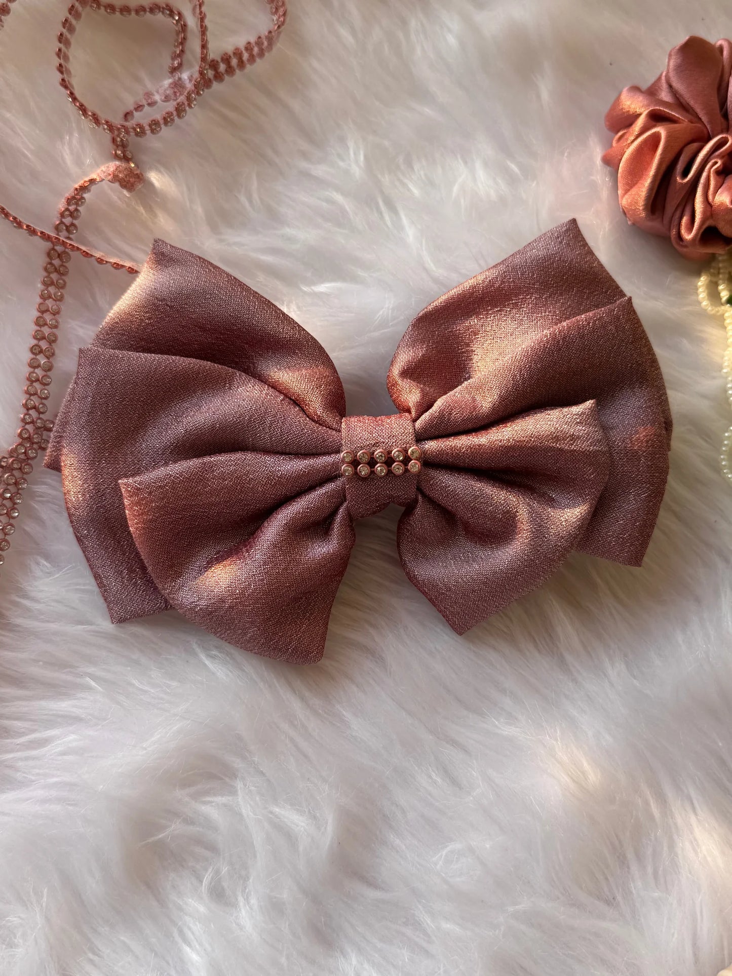 Rose gold silk hair bow with stone embellishment on white fur, handmade accessory by Bows and Bags India