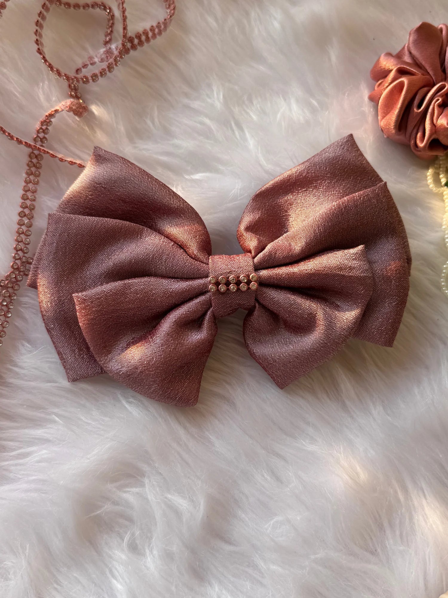 Rose gold silk hair bow with stone embellishment on white fur, handmade accessory by Bows and Bags India