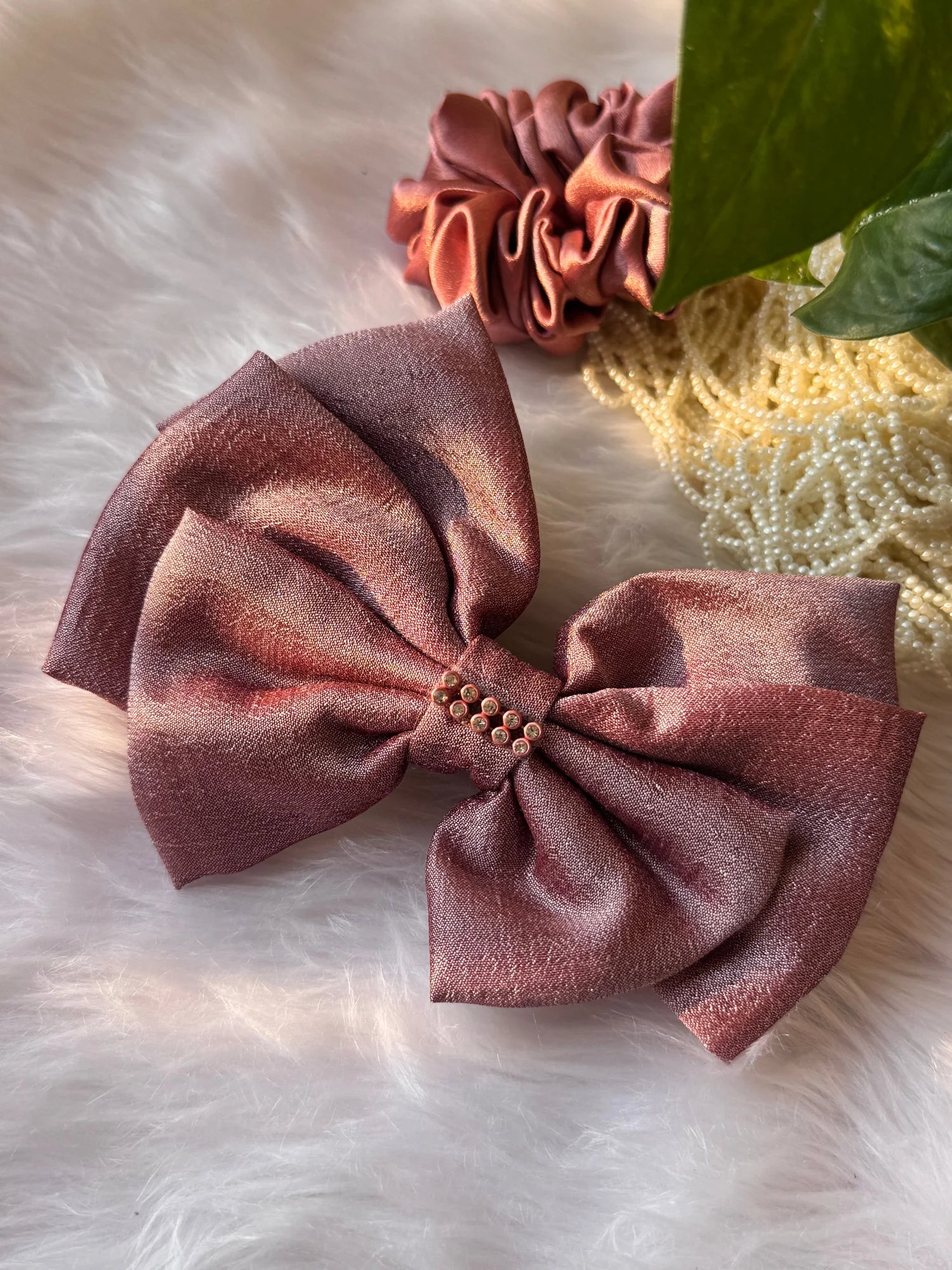 Rose gold silk hair bow with stone detailing from Bows and Bags India, displayed on white fur with matching scrunchie and