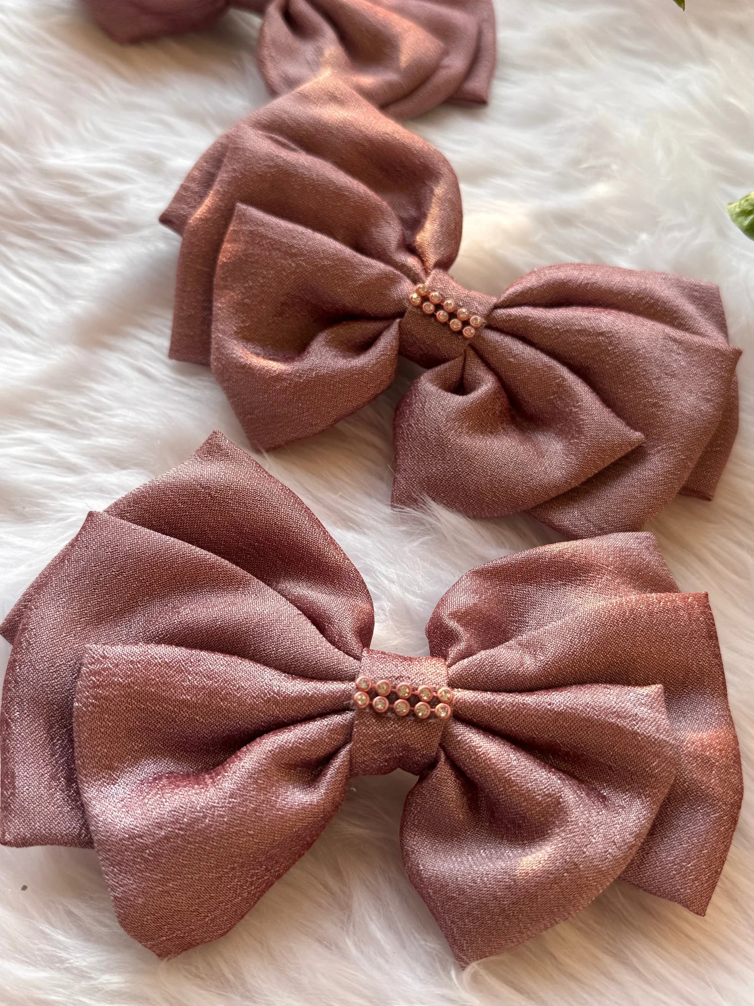 Rose gold silk hair bows with pearl stone embellishment by Bows and Bags India, handmade accessories displayed on white fur
